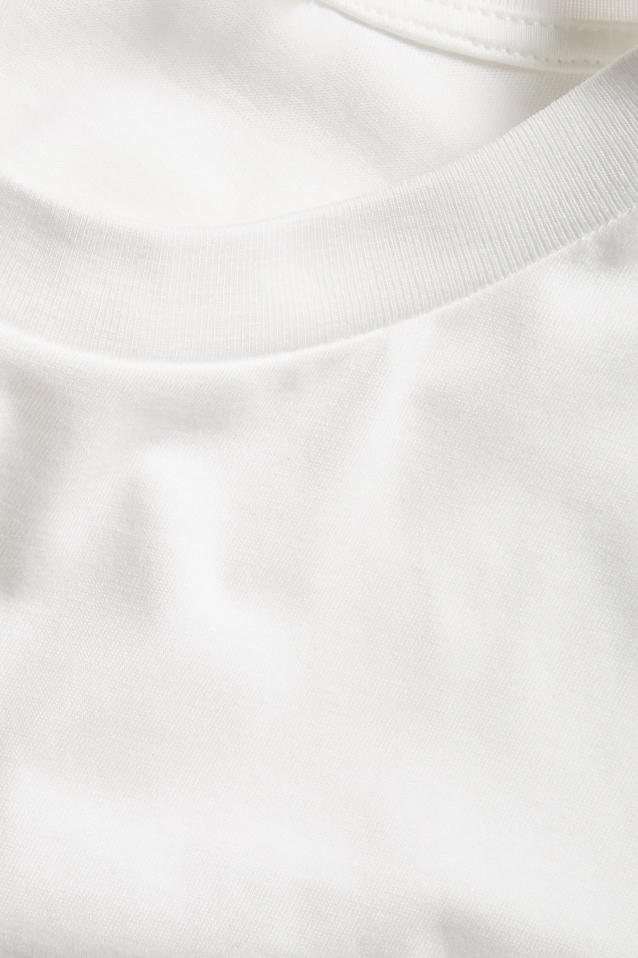 Zbliżenie na biały, oversize'owy bawełniany T-shirt, ukazujące gładki materiał i prążkowany dekolt.