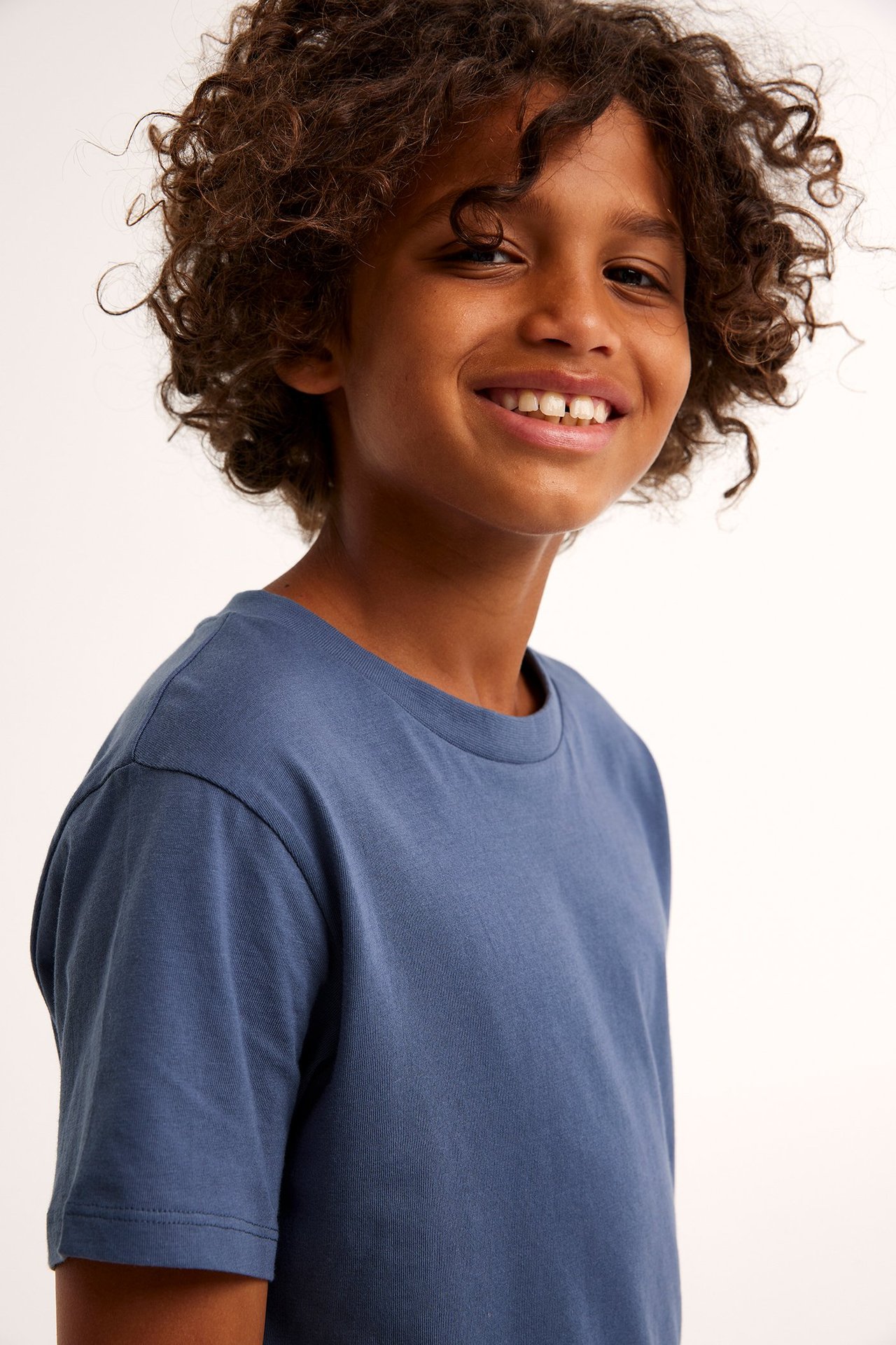 Framifrån, leende barn i mörkblå enfärgad t-shirt i bomull med ribbad rund halsringning.