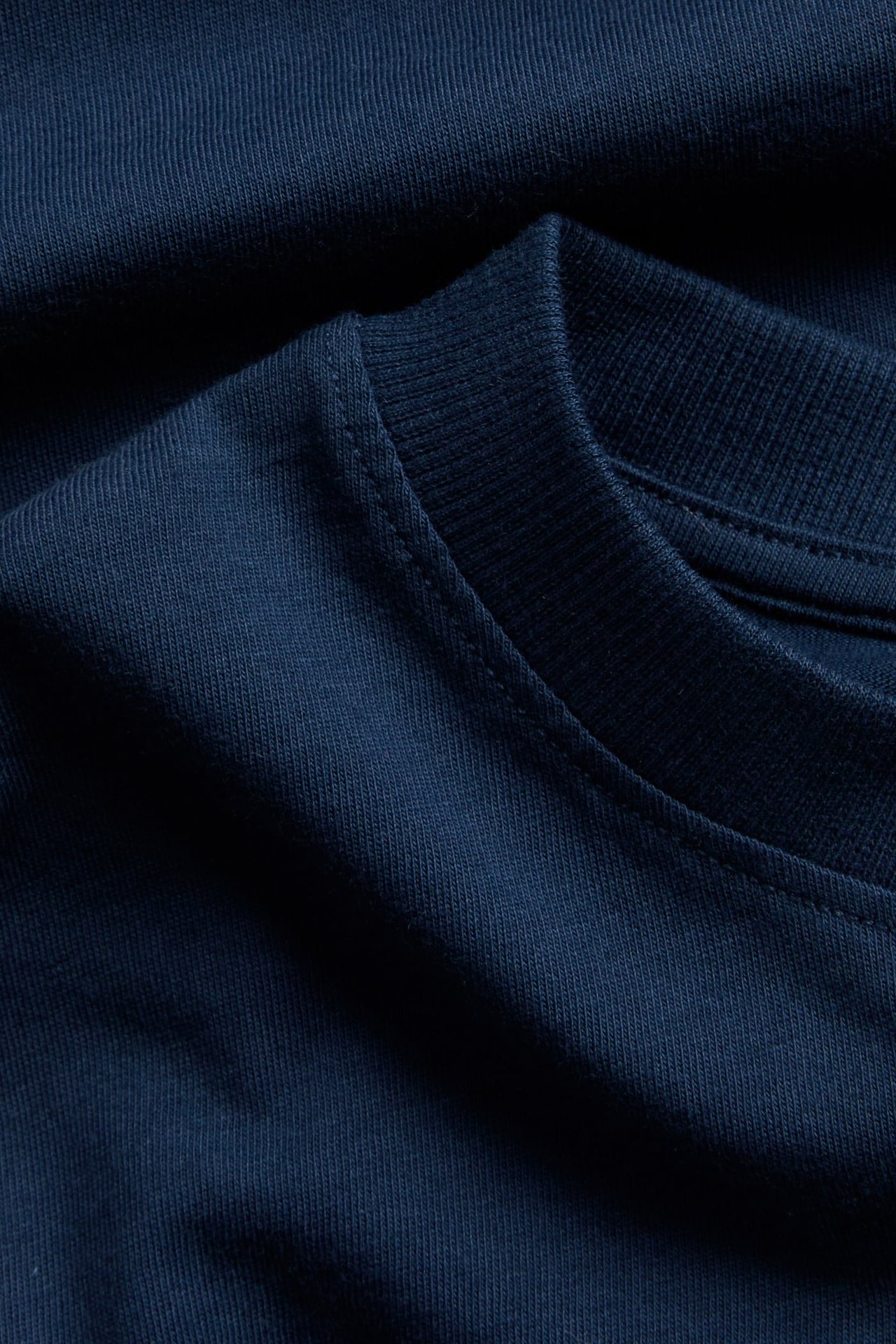 Zbliżenie na granatowy jednolity bawełniany T-shirt z prążkowanym dekoltem.