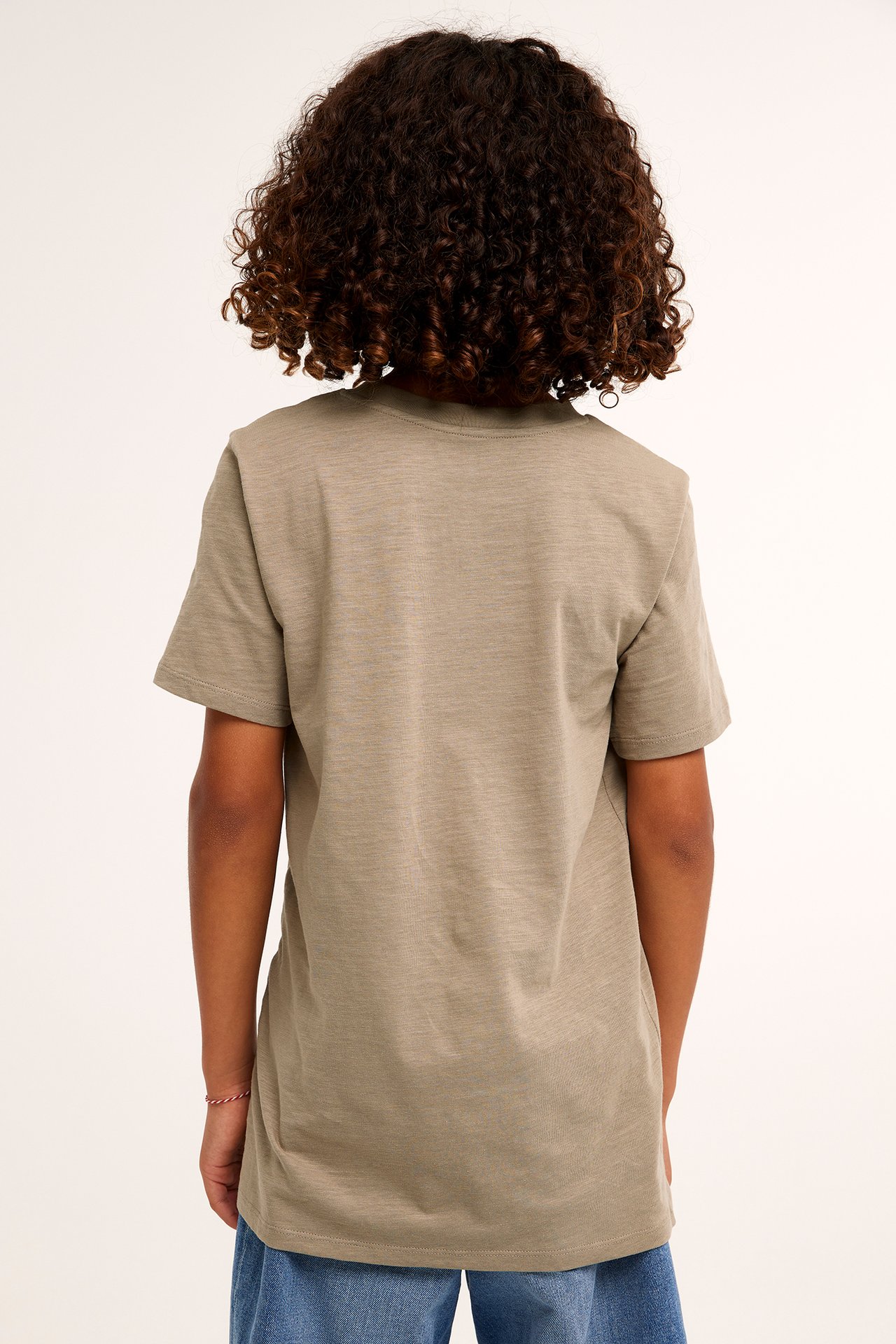 Bakifrån, ett barn i enfärgad brun bomulls-t-shirt och blå jeans.