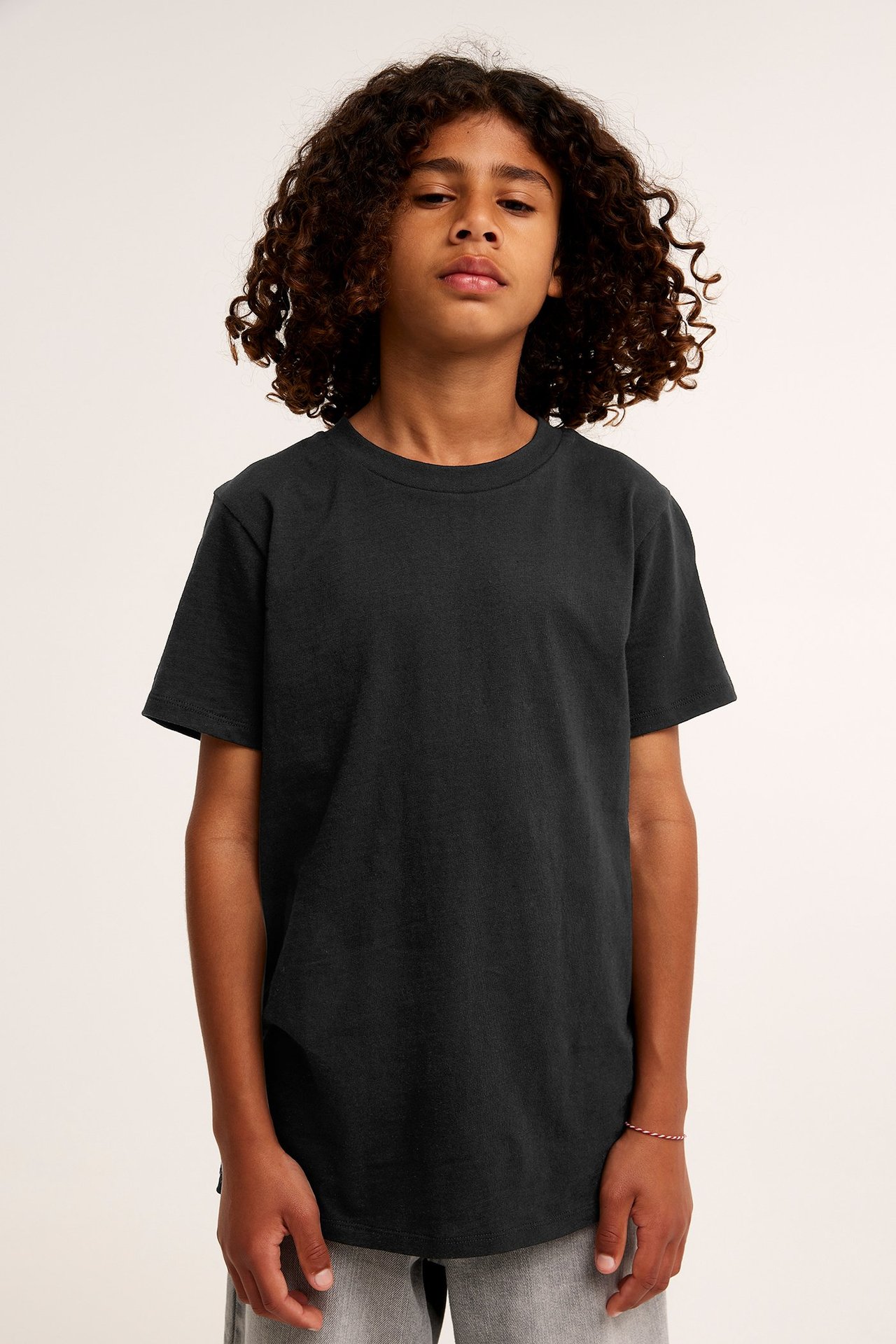 Frontvy av ett barn i en svart bomulls-t-shirt, grå byxor och ett rött och vitt armband.