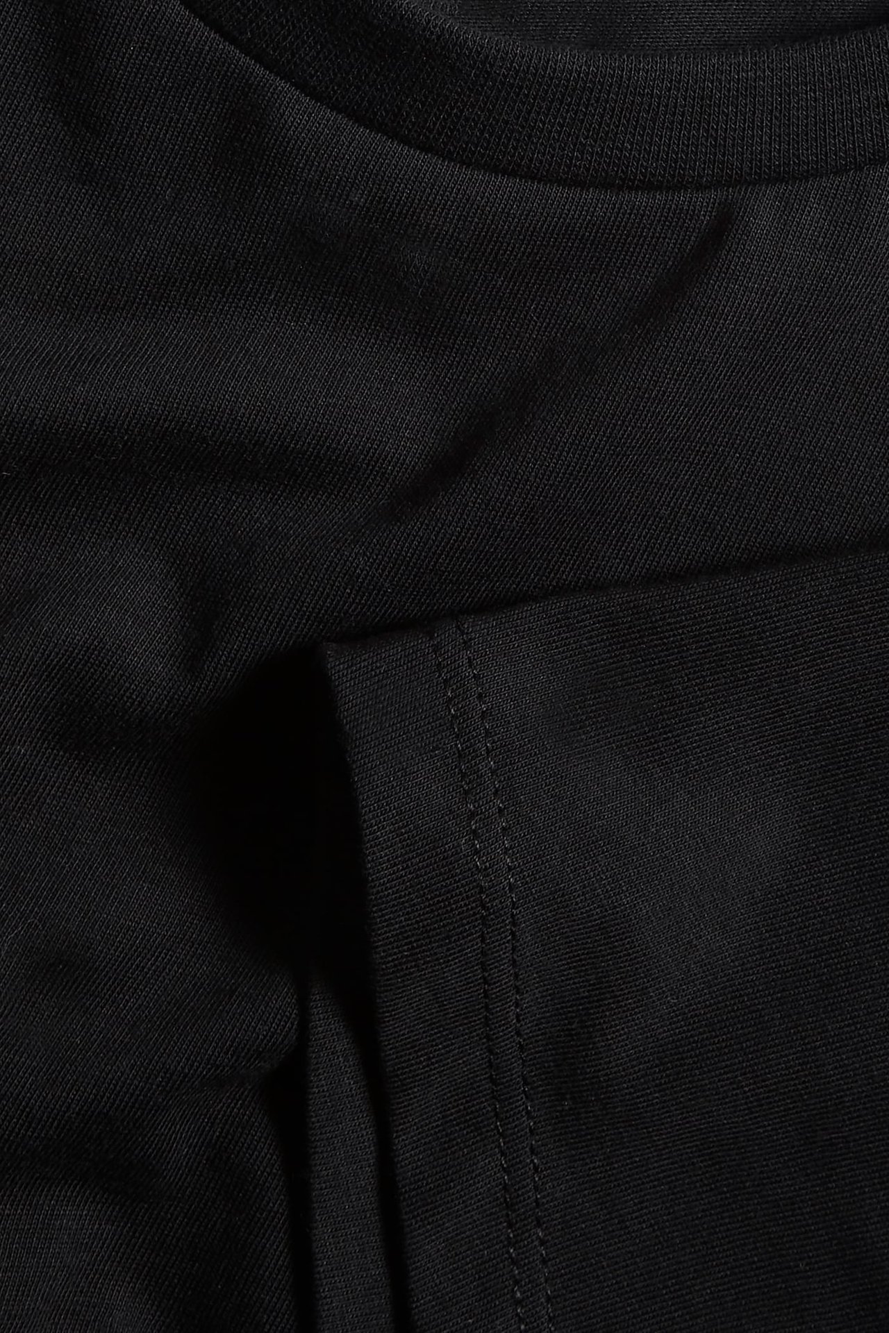 Zbliżenie czarnego bawełnianego t-shirtu z prążkowanym dekoltem i widocznym szwem na rękawie.