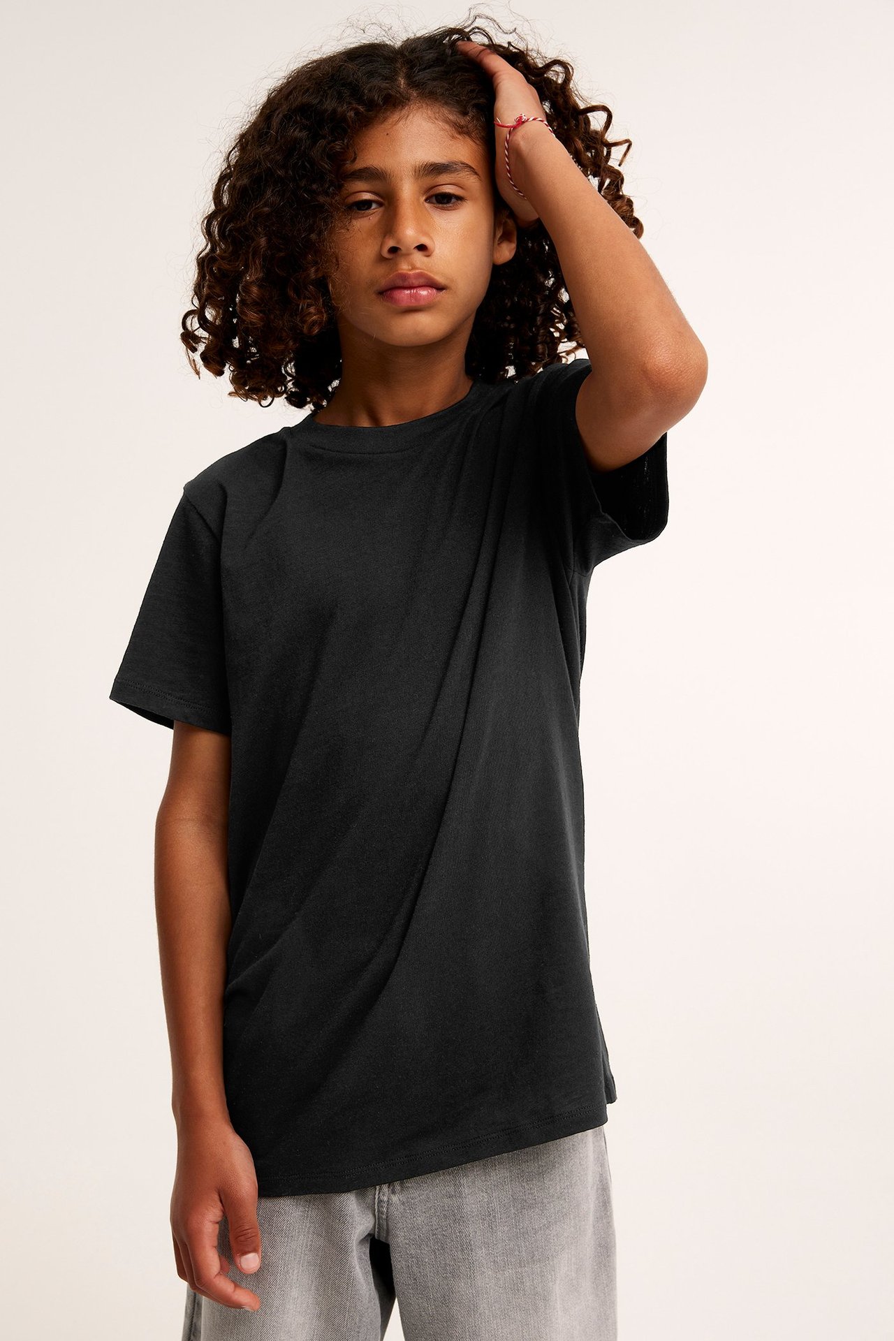 Frontvy av ett barn i en svart bomulls-t-shirt, grå shorts och ett randigt armband.