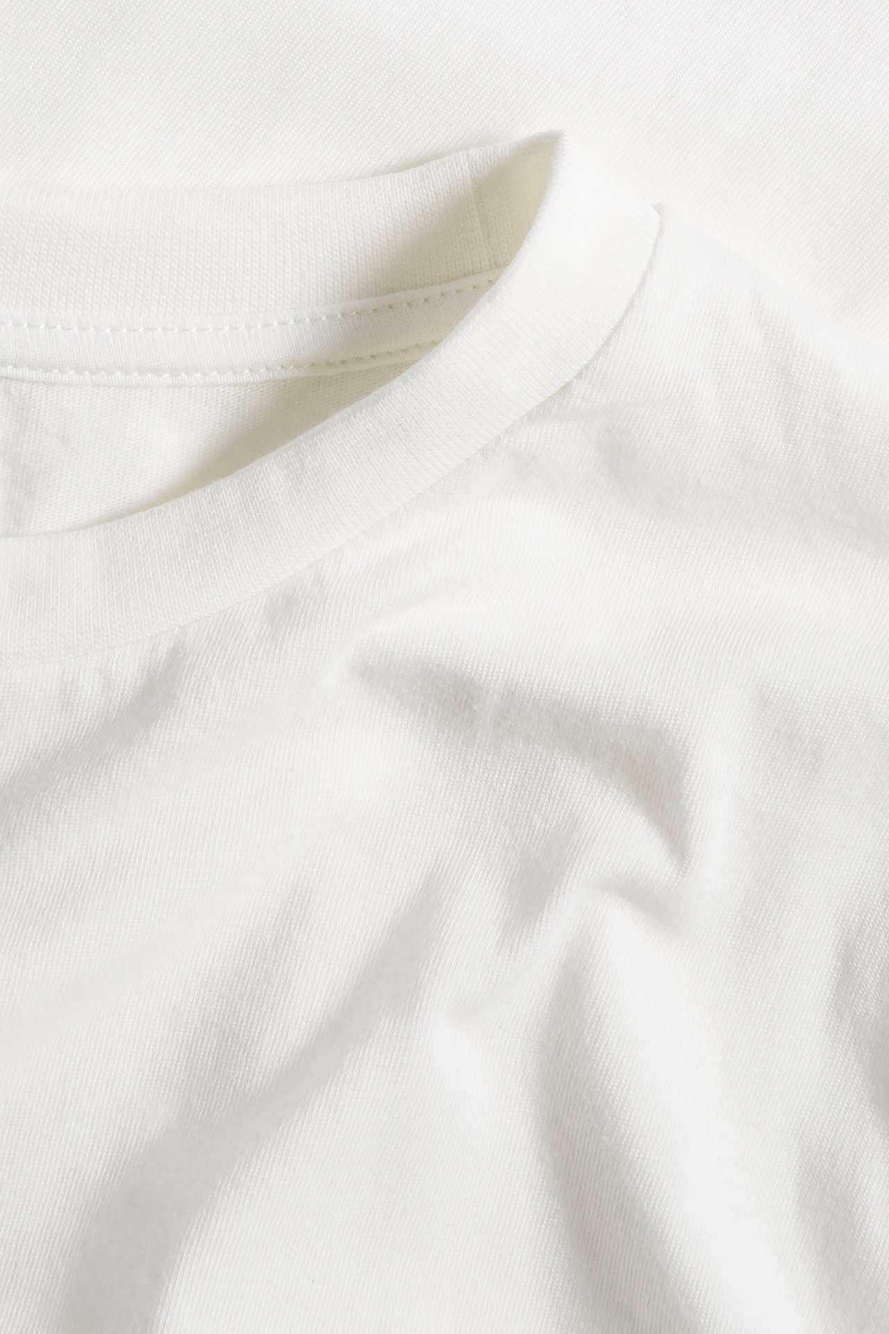 Närbild av en offwhite t-shirt i bomull med ribbad rund halsringning och mjuk tygstruktur.
