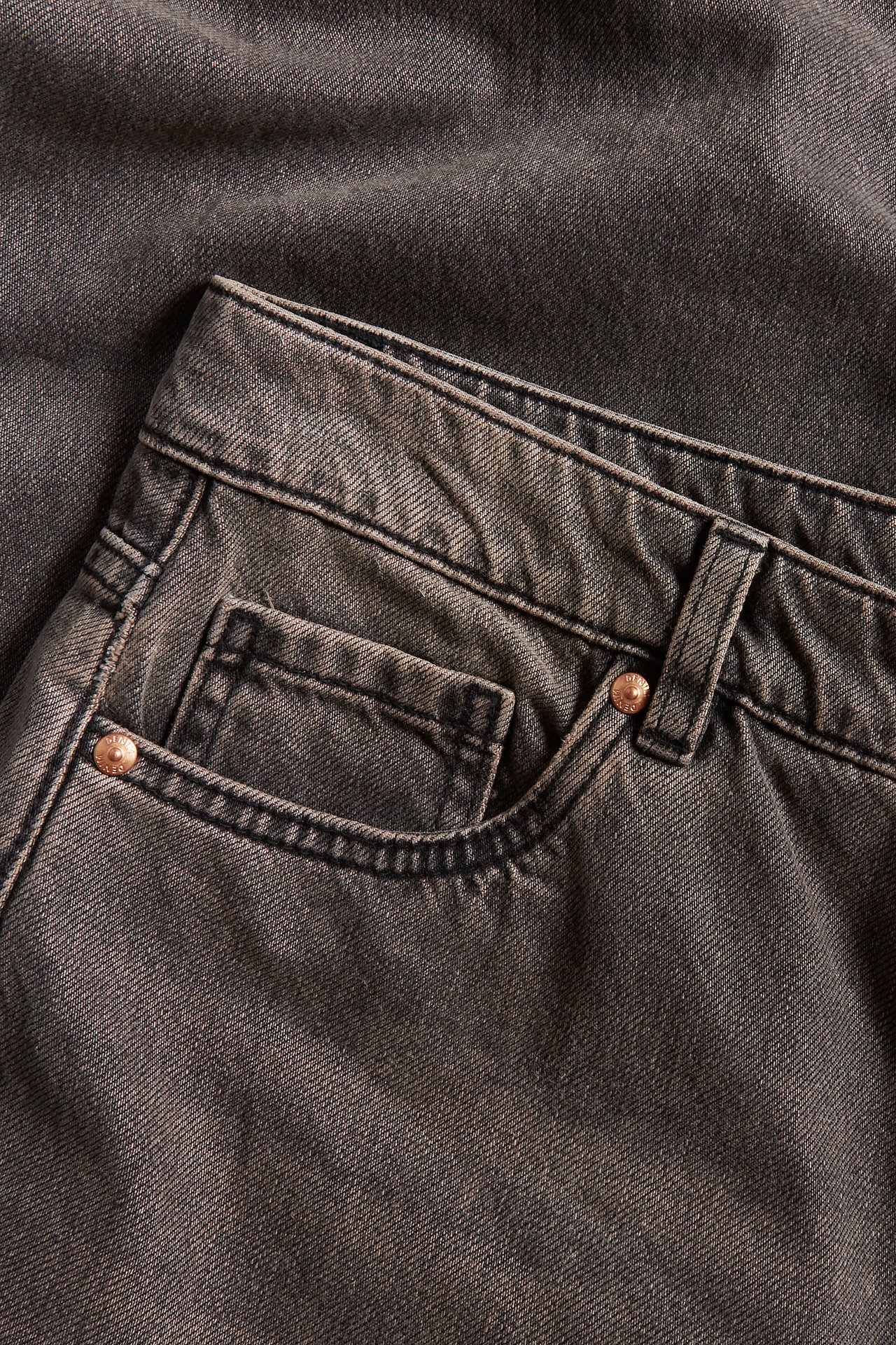 Närbild av tvättade svarta bomulls-baggy jeans med normal midja, fickor och kopparfärgade nitar.