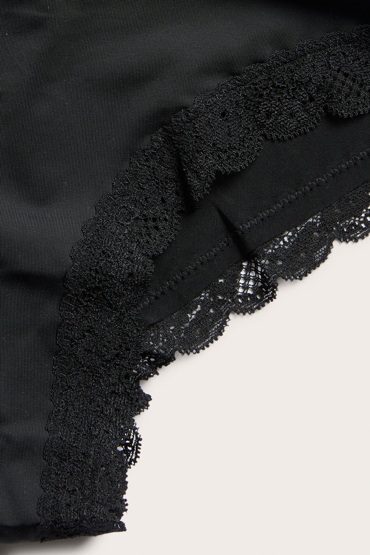 Lähikuva mustista mikrokuituisista cheeky-alushousuista, joissa pitsireuna vyötäröllä ja lahkeissa.