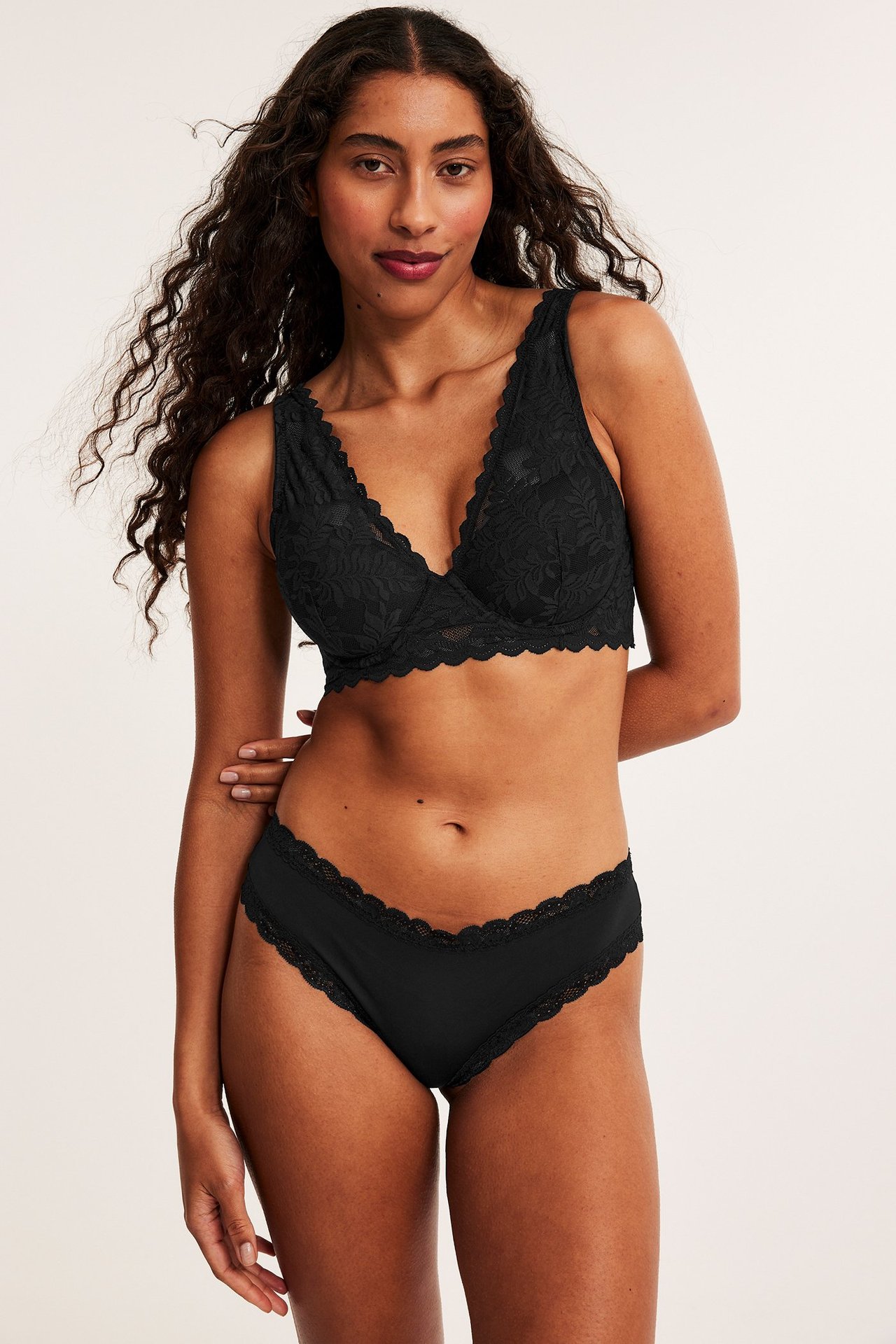 Forfra, kvinne i svarte cheeky truser med blondekant og matchende svart blondebralette.