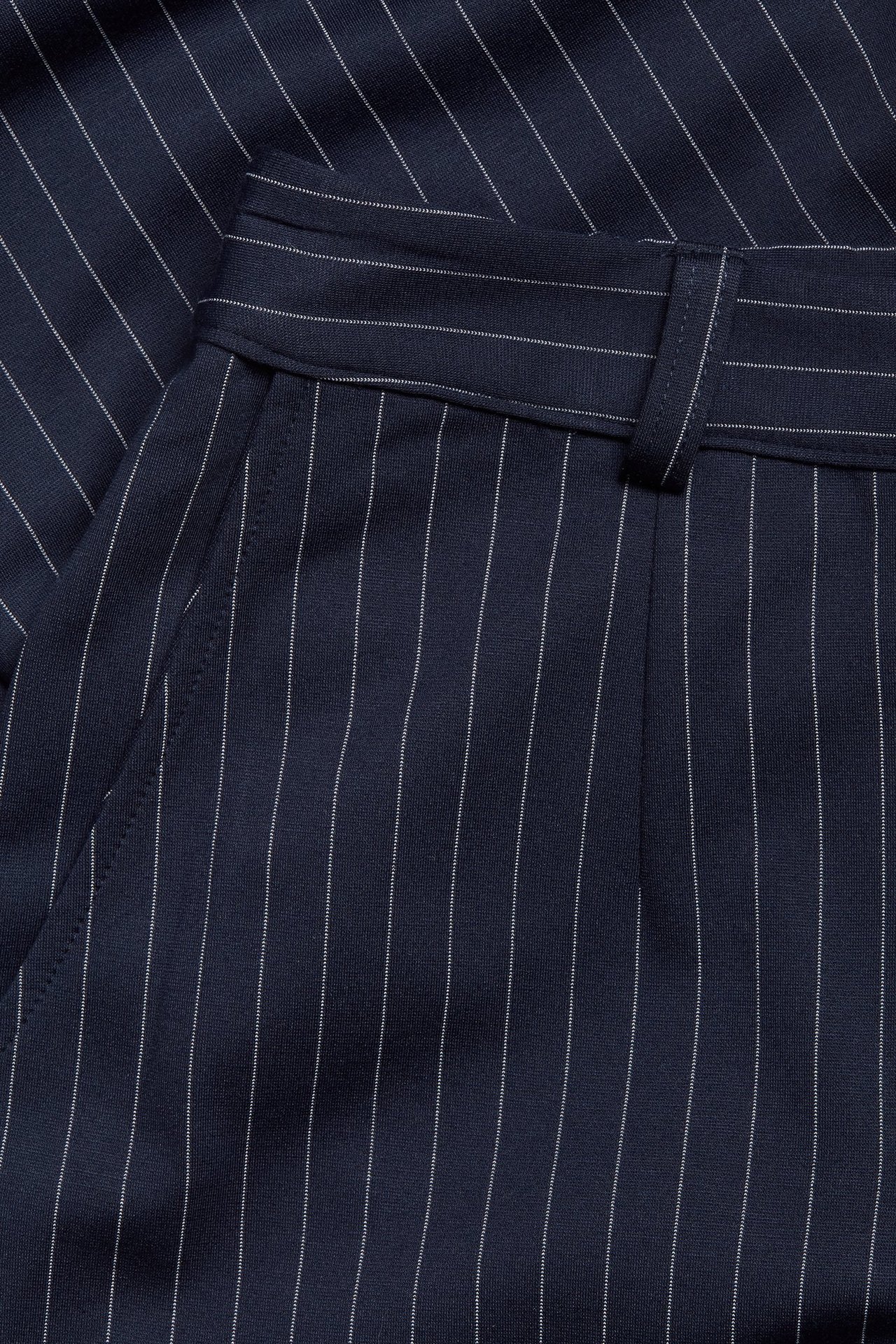 Zbliżenie na granatowe spodnie garniturowe w prążki z kieszenią i szlufką.