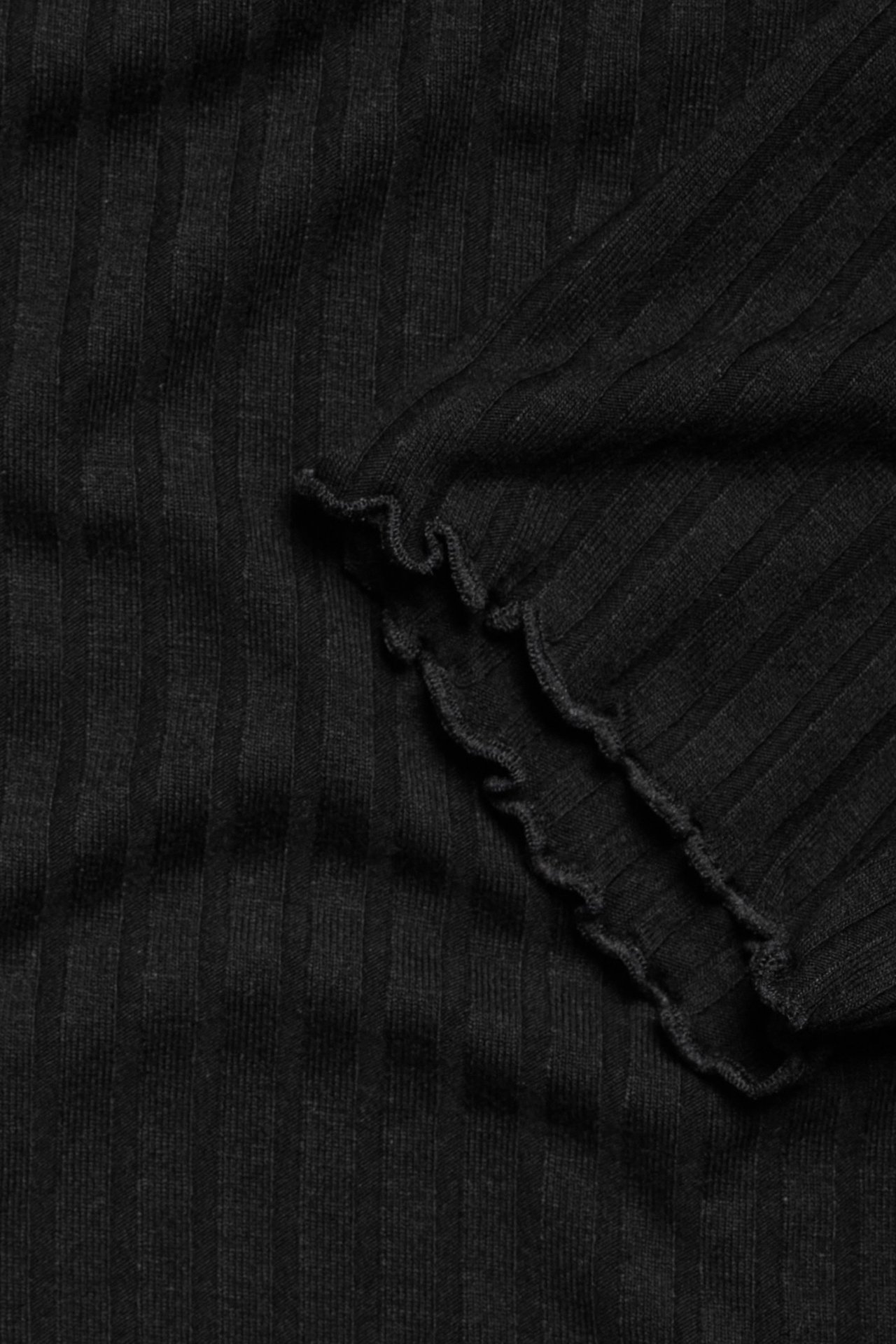 Zbliżenie czarnej prążkowanej sukienki z dzianiny z falbankowym brzegiem.