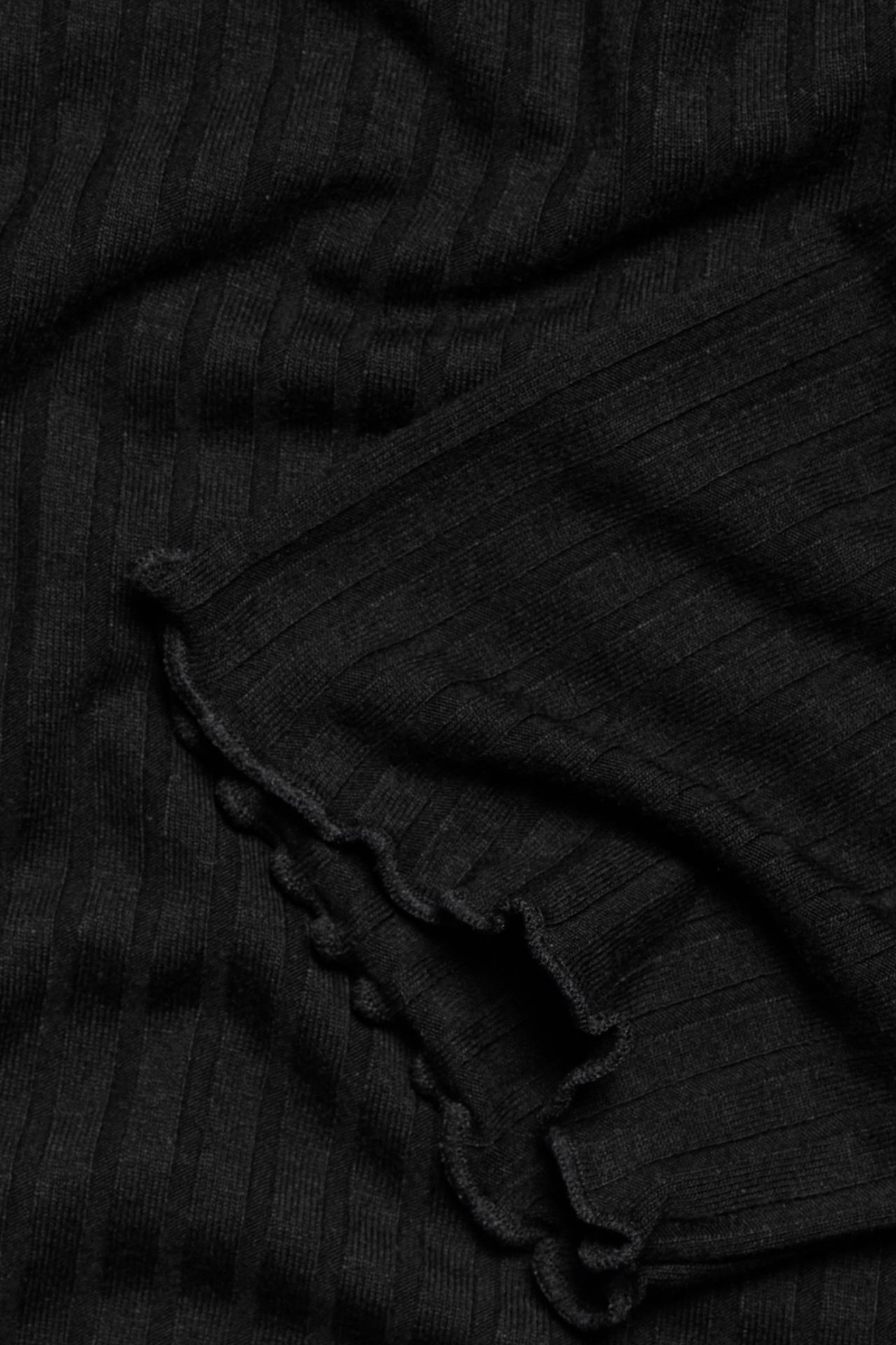 Zbliżenie czarnej prążkowanej tuniki z dzianiny z falbankami.