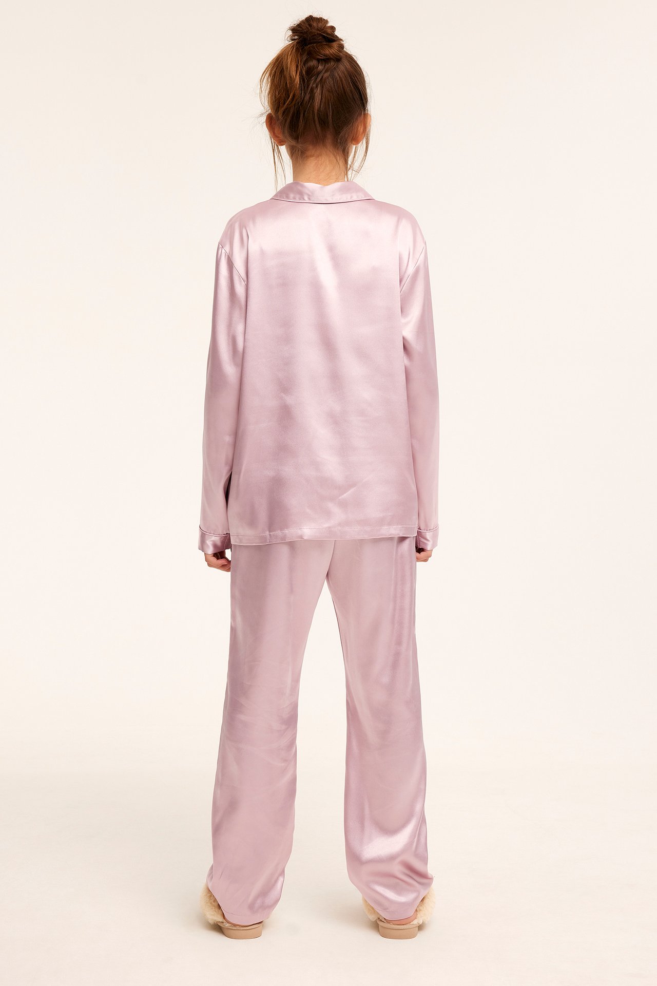 Bakifrån: ett barn i rosa satinpyjamas och fluffiga tofflor.