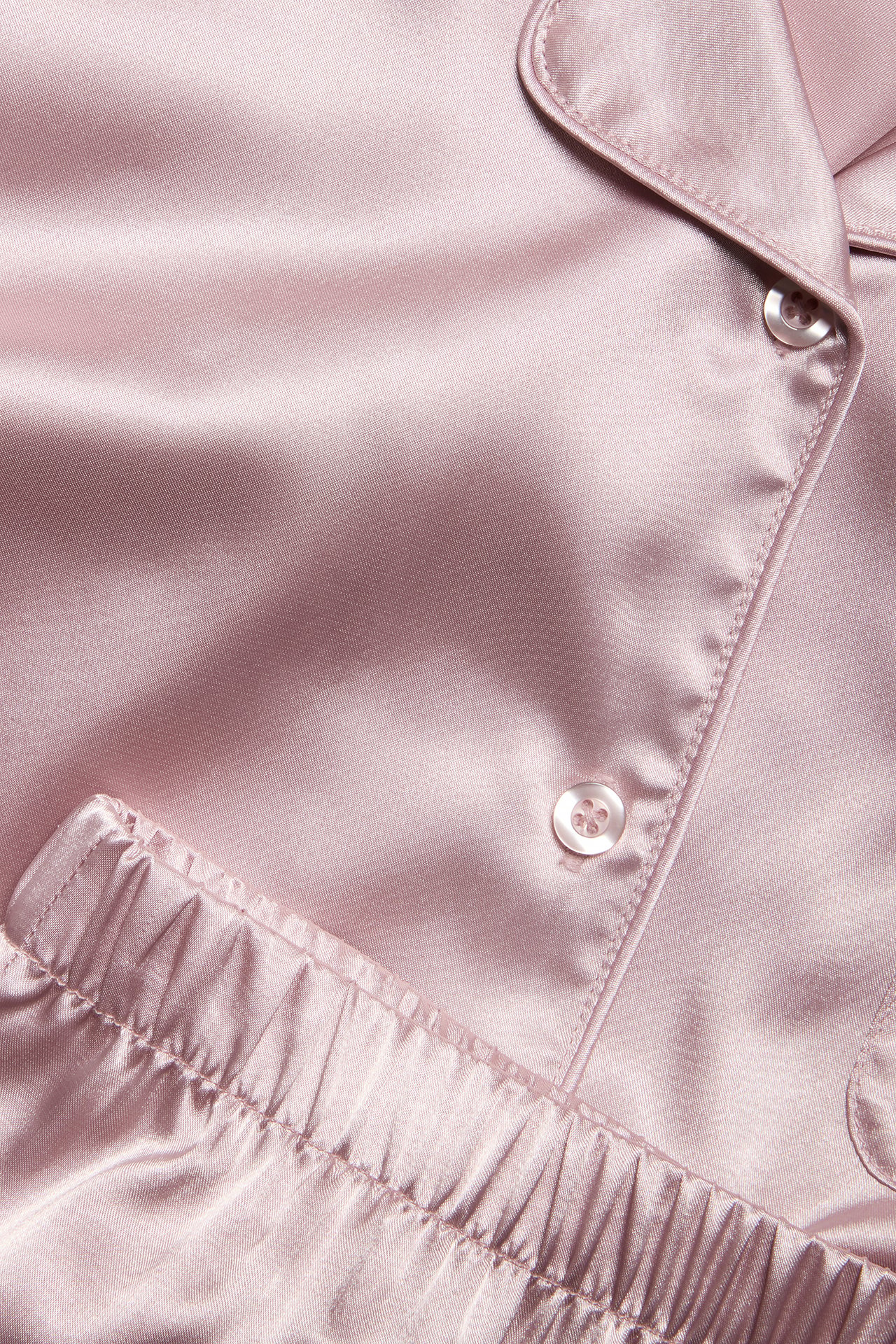 Närbild av rosa satinpyjamasöverdel med knappar och resår i midjan på pyjamasbyxan.