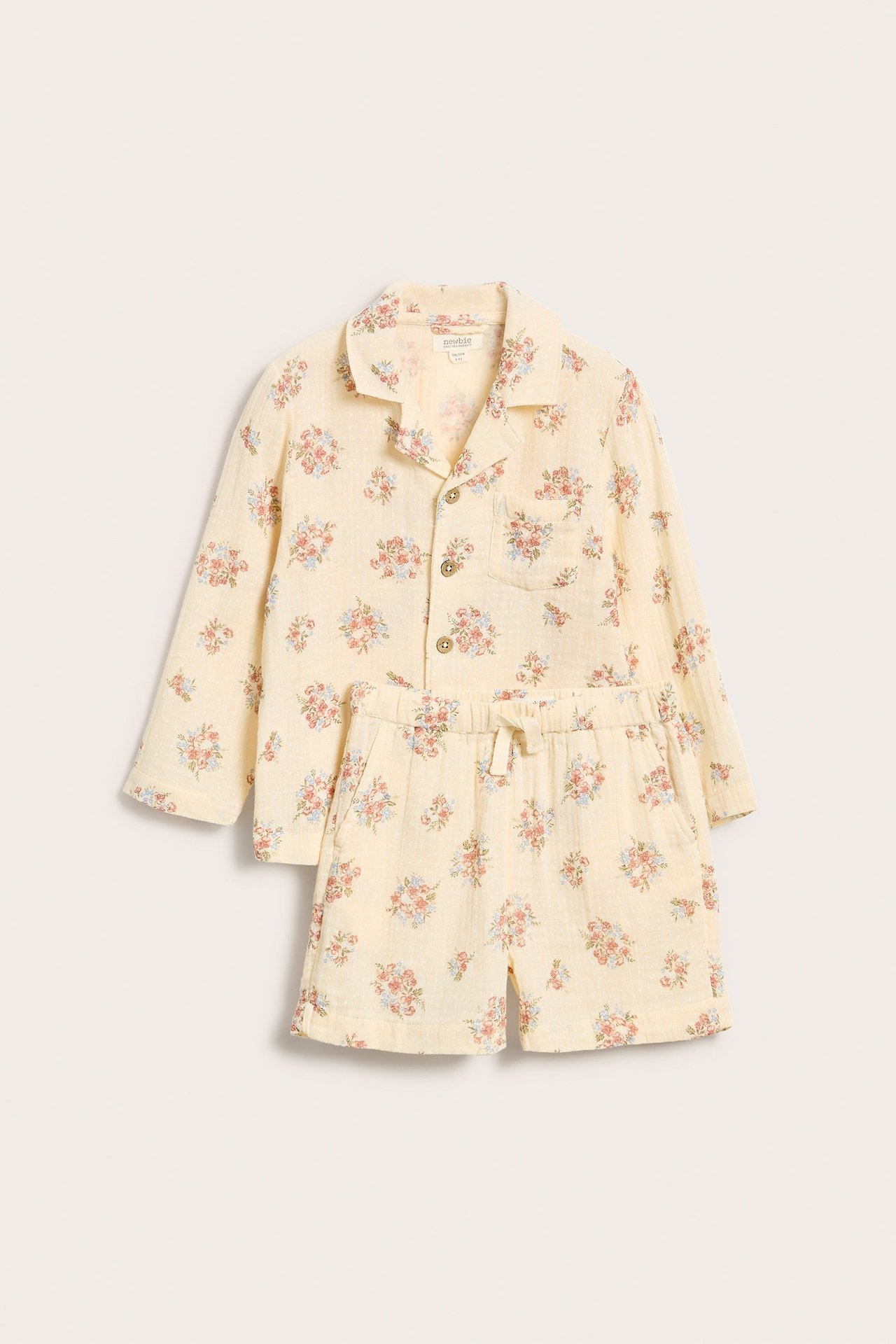Edestä vaaleankeltainen kukkakuvioinen kudottu puuvillapyjamassetti, jossa pitkähihainen paita ja shortsit.
