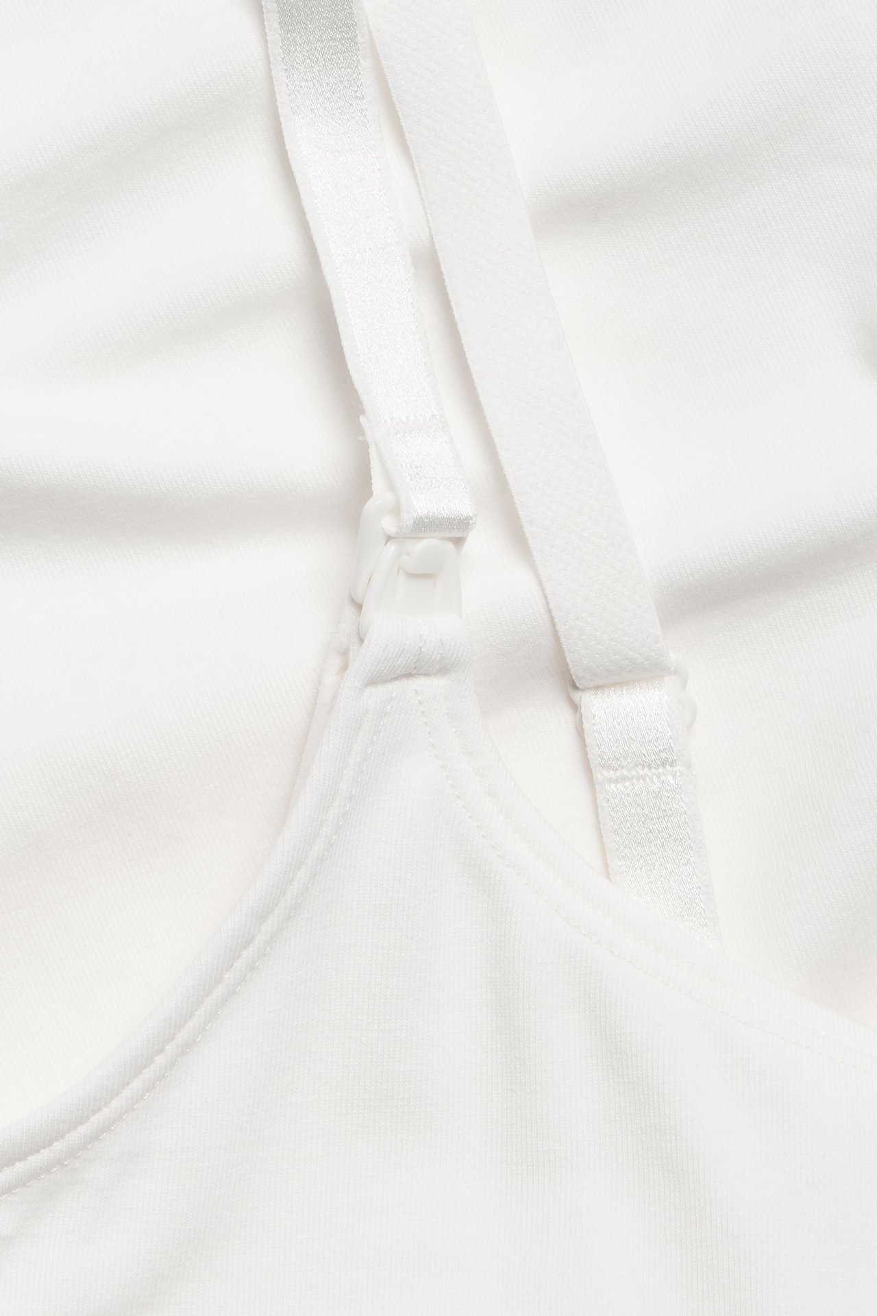 Zbliżenie na biały top do karmienia z bawełny organicznej z regulowanym ramiączkiem i zapięciem.