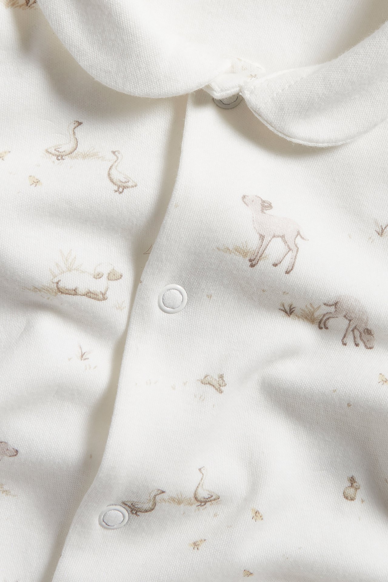 Närbild framifrån: offwhite babypyjamas med rund krage, brunt djurmönster och tryckknappar.