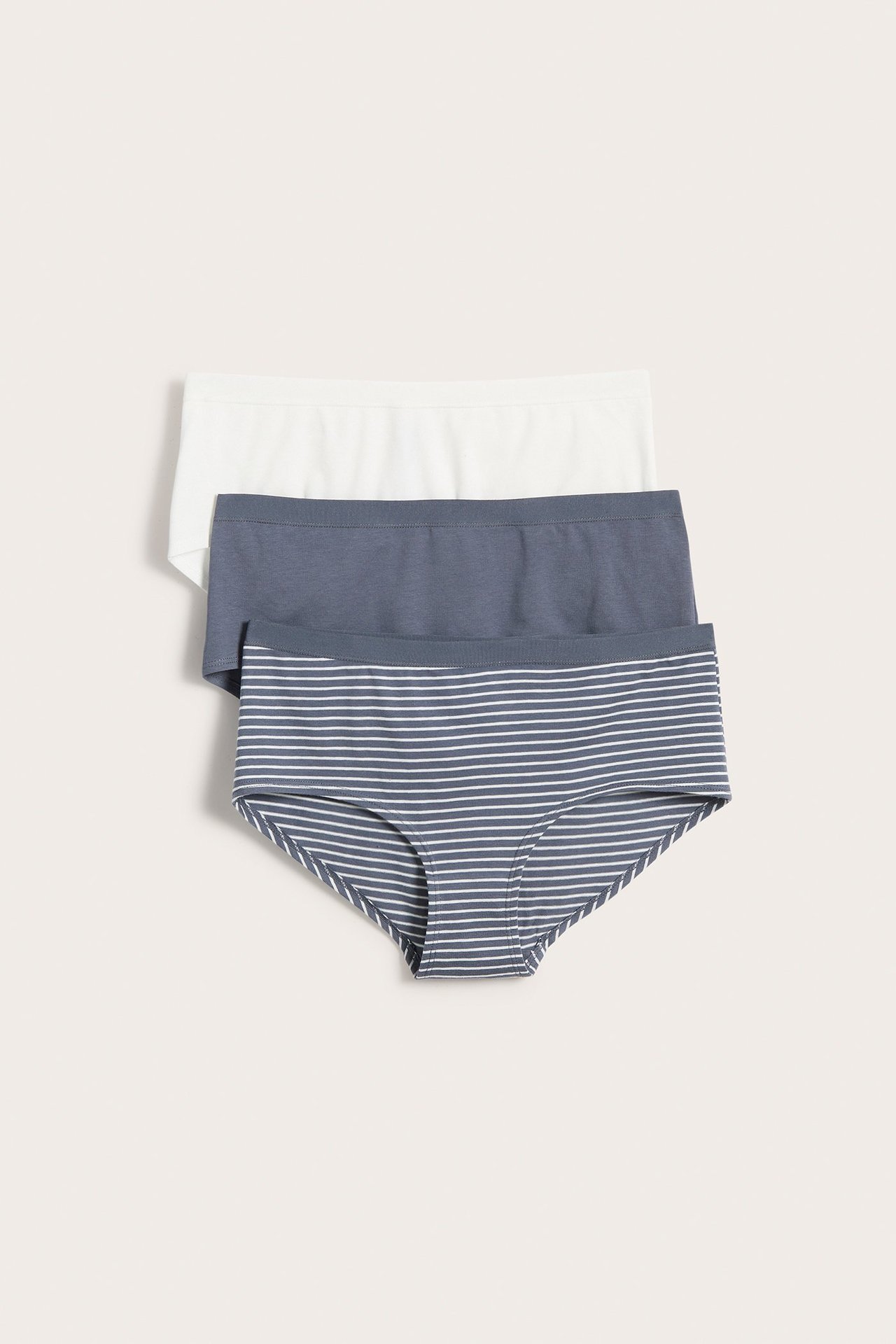 Ovenfra sett, tre bomullshipsttruser for dame: en stripete gråblå, en ensfarget gråblå og en hvit.