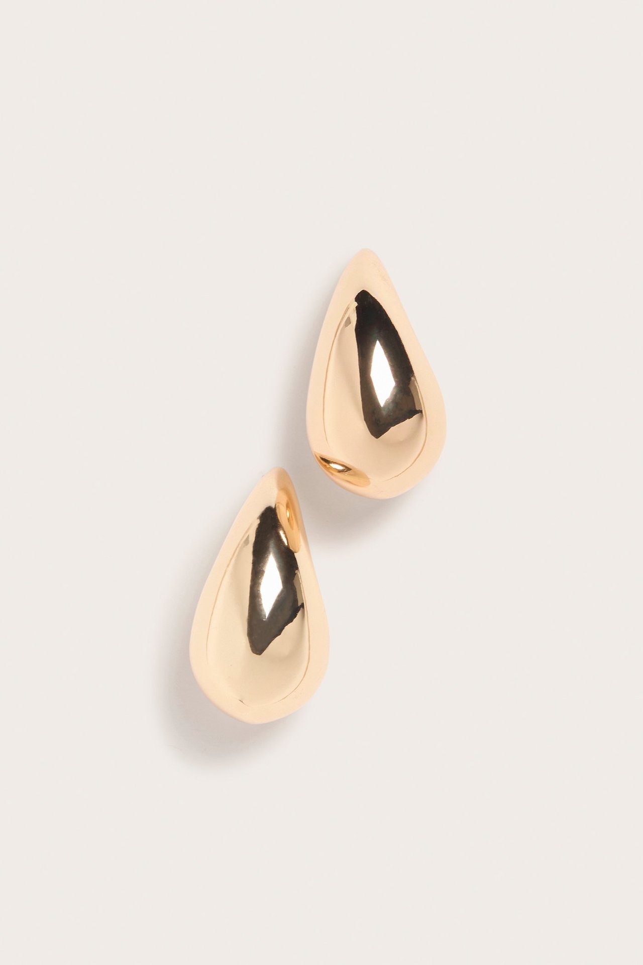 Närbild av två glänsande guldfärgade droppformade örhängen med reflekterande yta.