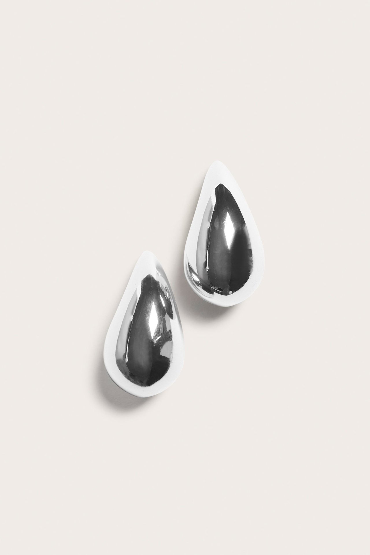 Toppvy av ett par glänsande silverfärgade droppformade örhängen, 3 cm långa.