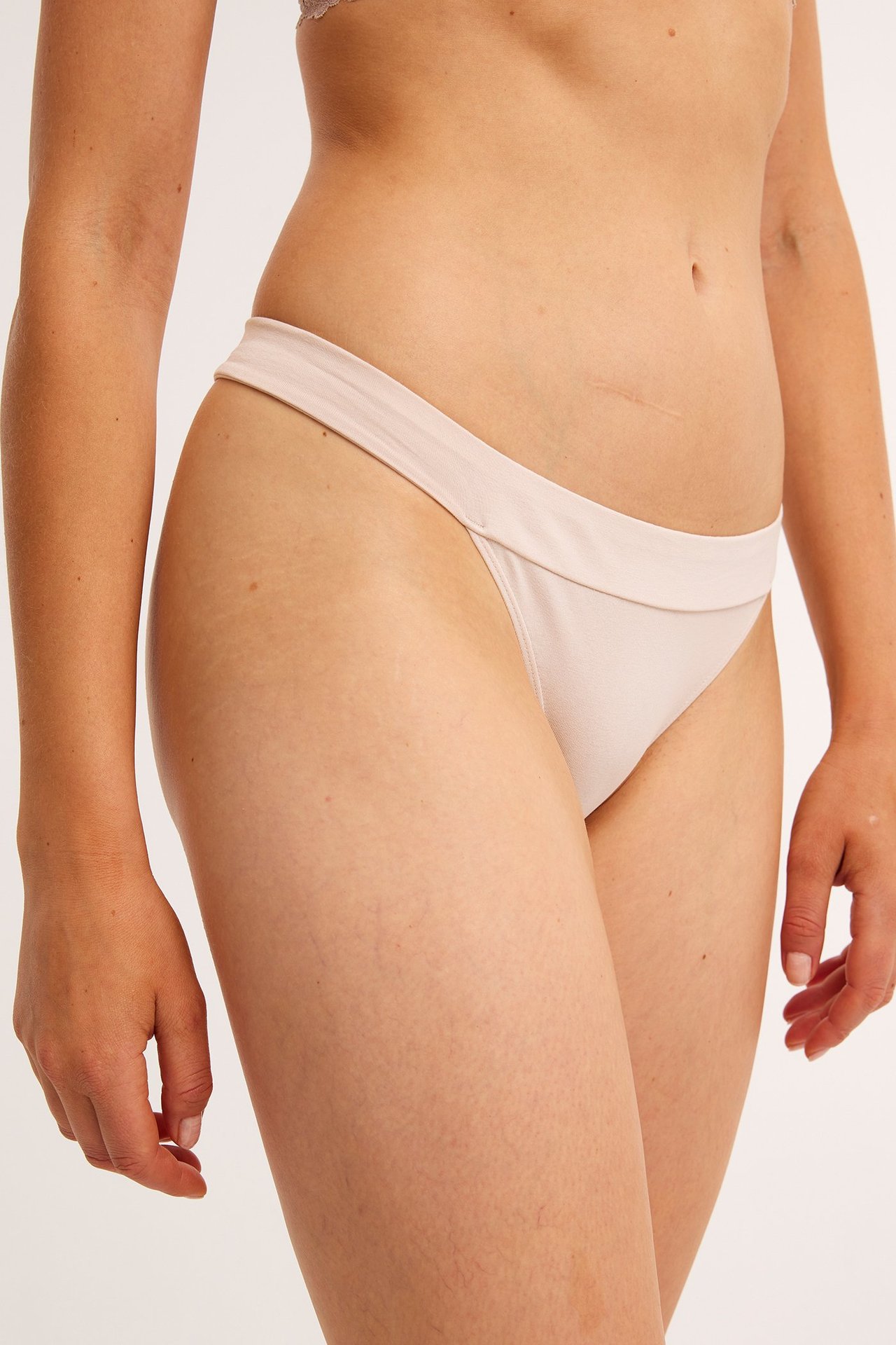 Sidebilde av en kvinne i lys rosa stringtruse i bomullsblanding og matchende BH.