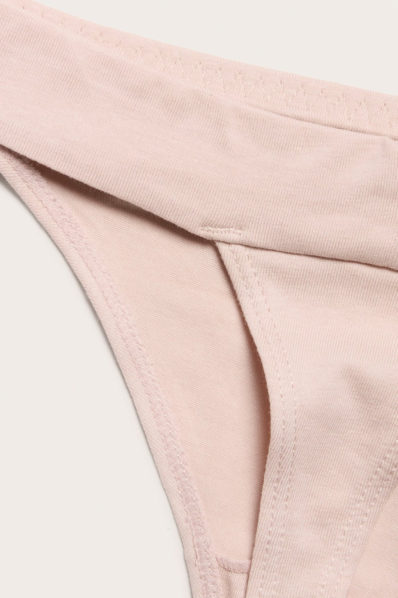 Zbliżenie na jasnoróżowe, gładkie stringi z mieszanki bawełny, z prążkowaną fakturą i widocznymi szwami.