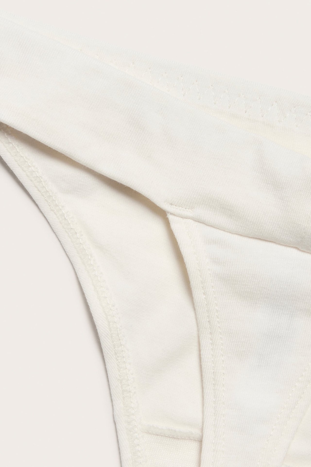 Zbliżenie białych, jednolitych majtek stringów z mieszanki bawełny z widocznymi szwami.