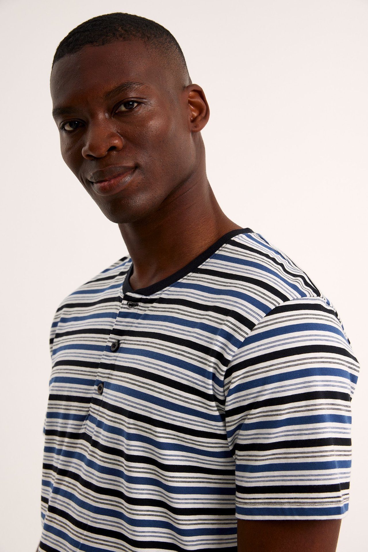 Lähikuva miehestä raidallisessa puuvillapyjamapaidassa, jossa sinisiä, mustia, valkoisia ja vaaleanbeigen raitoja, napeilla.