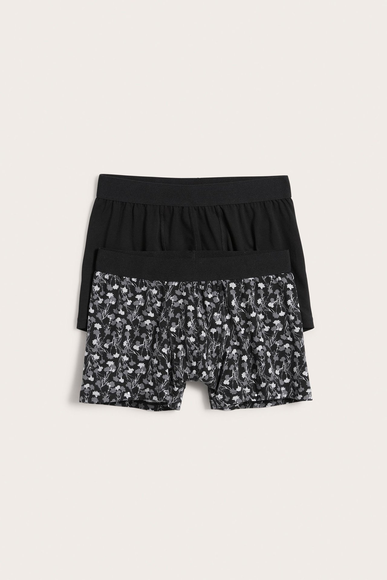 Widok z przodu dwóch bokserek męskich: jedne czarne w szary kwiatowy wzór, drugie jednolicie czarne.