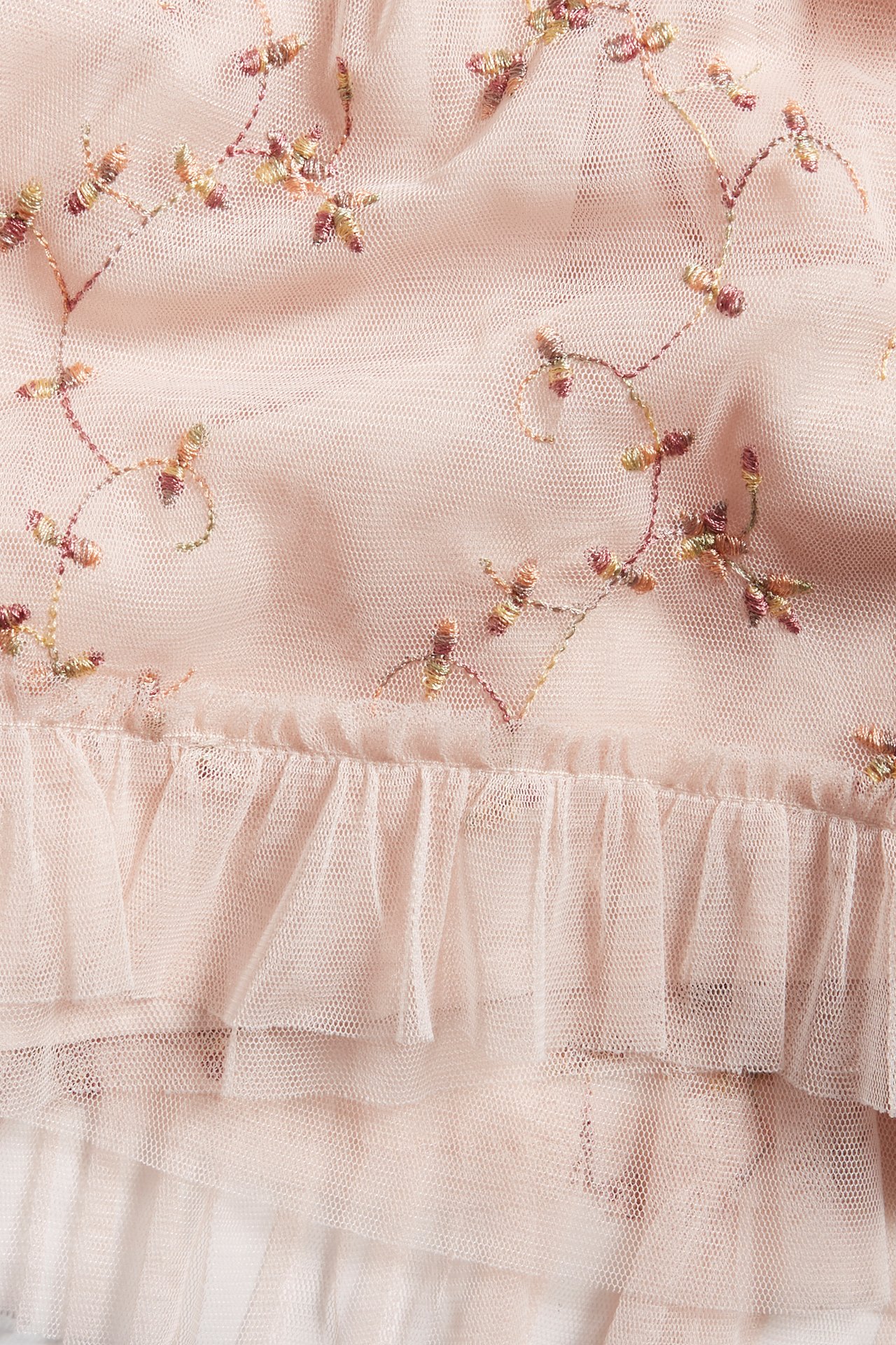 Nærbilde av en lys rosa babykjole med flerfarget blomsterbroderi og volangdetaljer i mesh.
