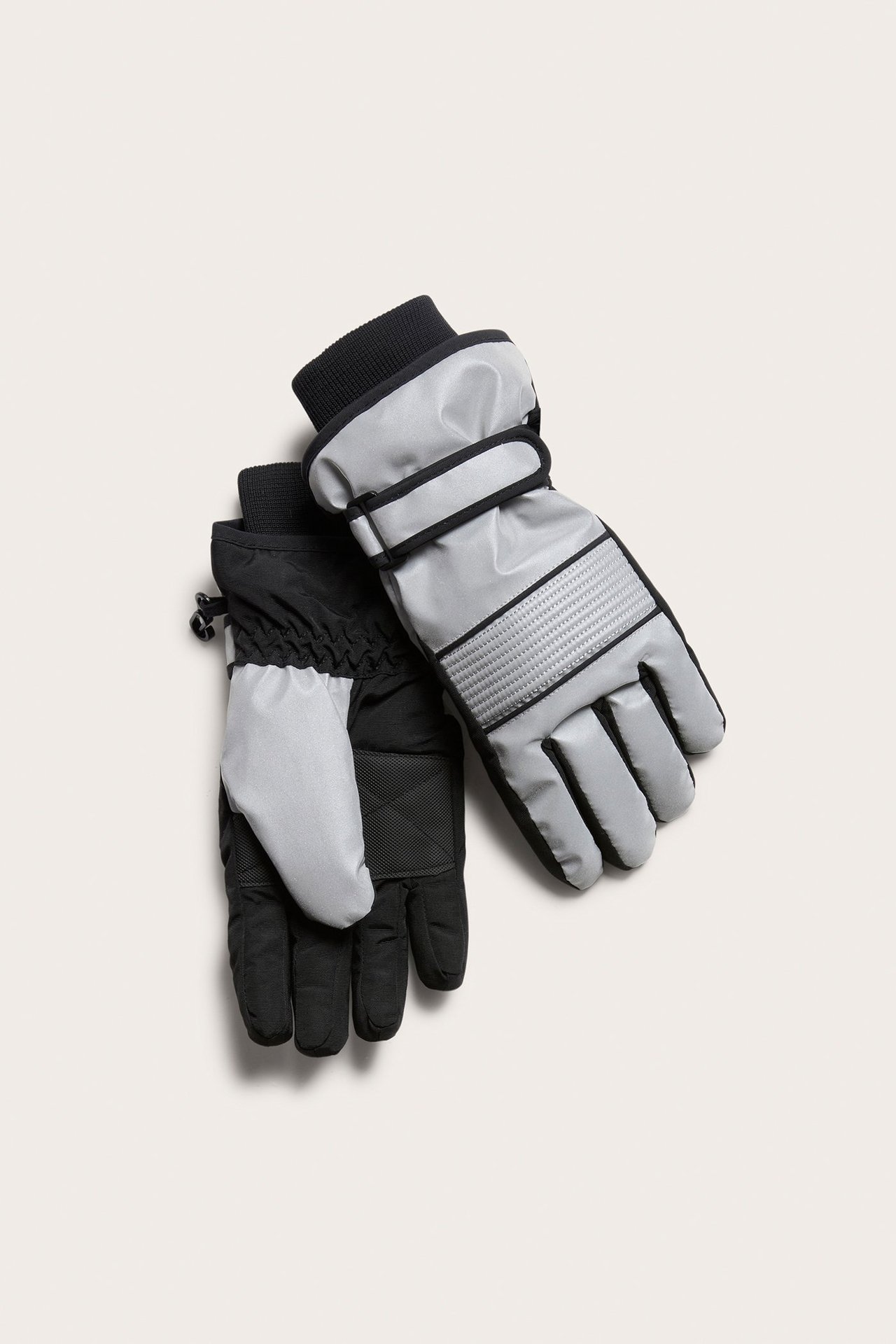 Ylhäältä kuvattu pari lasten hopeisia heijastavia talvihanskoja mustilla kämmenillä, resoreilla ja rannehihnoilla.