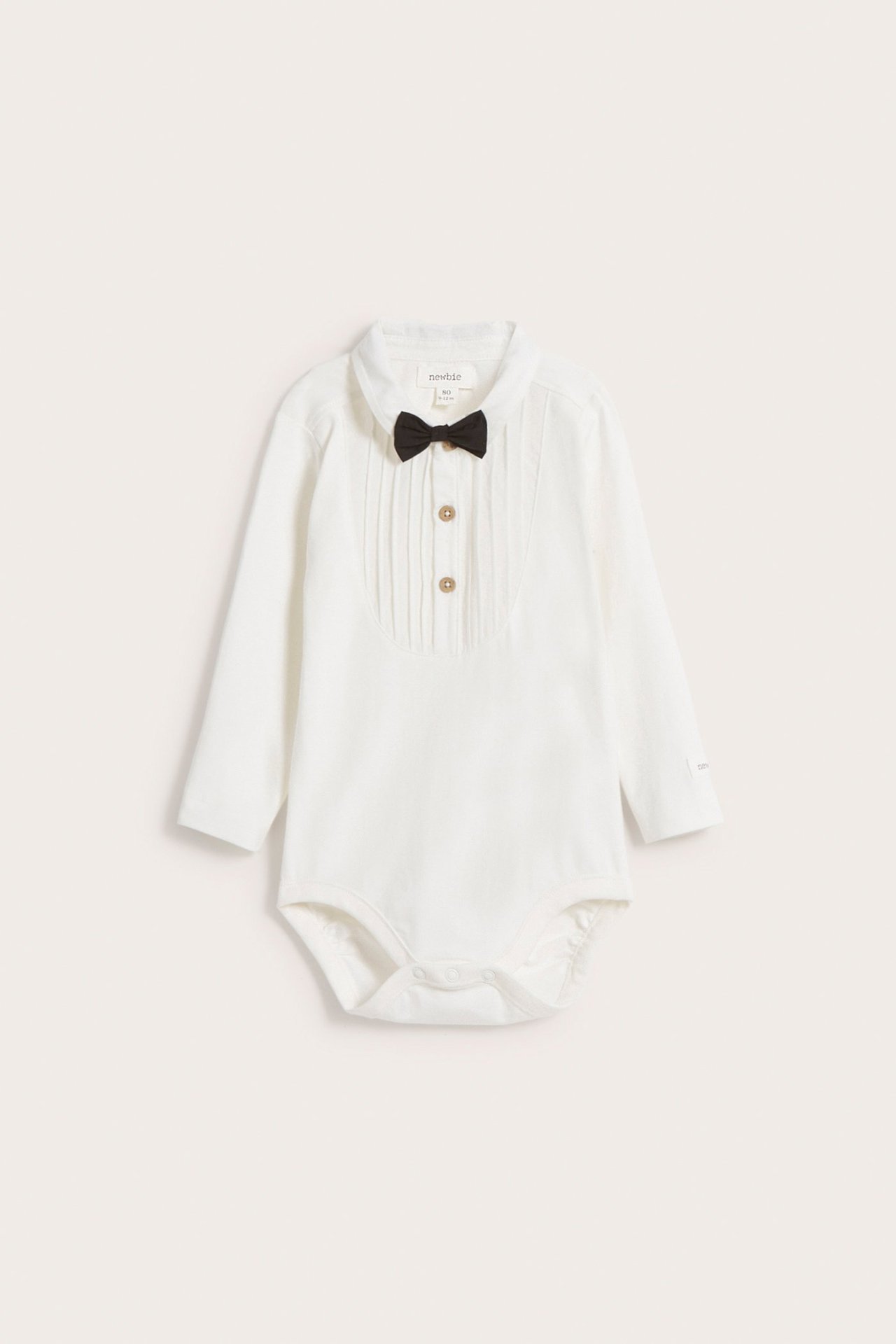 Forfra: offwhite langermet babybody med plissert front, knapper og svart sløyfe.