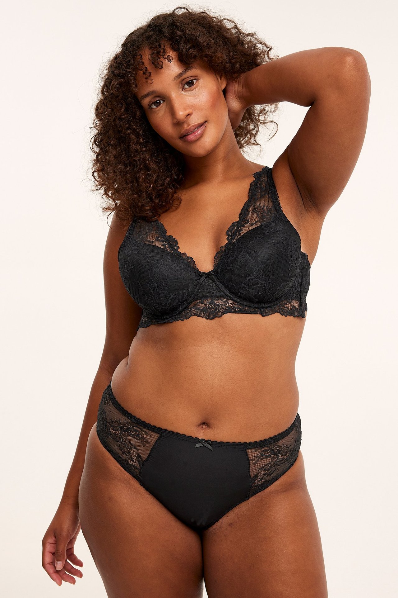 Frontbilde av en kvinne i svarte blonde-briefstruser med mikrofront og matchende svart blonde-BH.