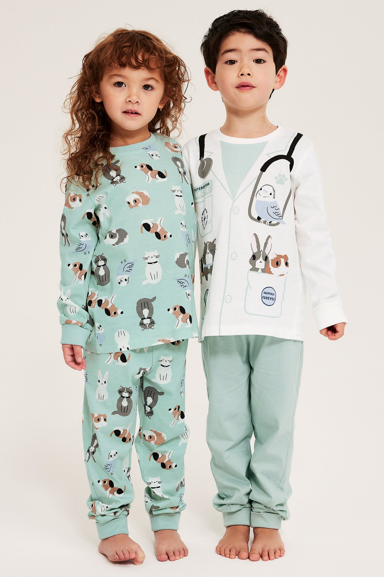 Widok z przodu dwóch dzieci w bawełnianych piżamach: jedne jasno turkusowe w zwierzęta, drugie białe i jasno turkusowe weterynaryjne.