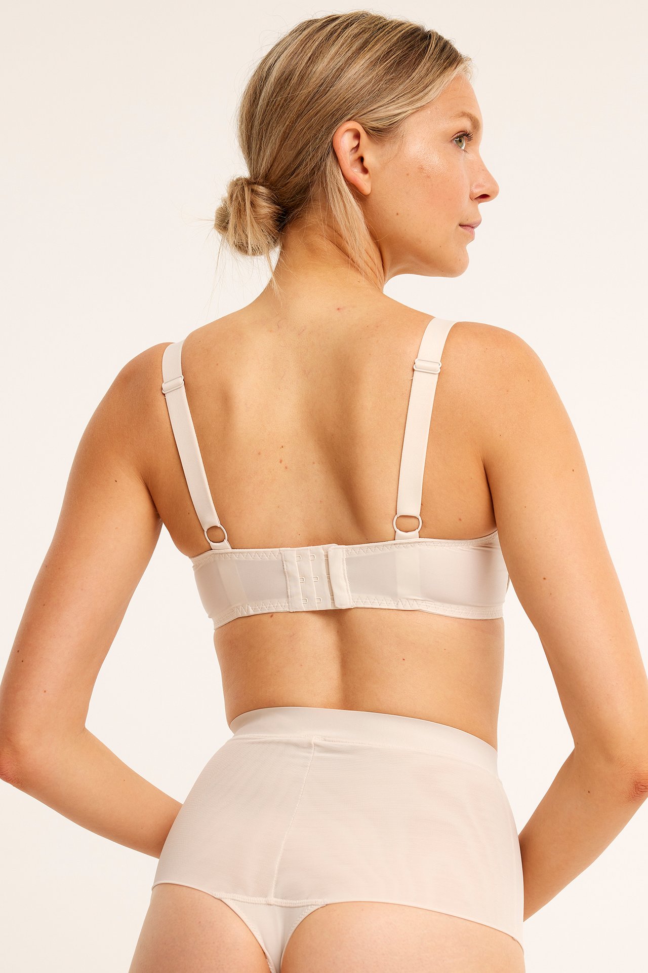 Bakifrån: kvinna i beige minimizer-bh med hak- och hyskknäppning och matchande trosa.