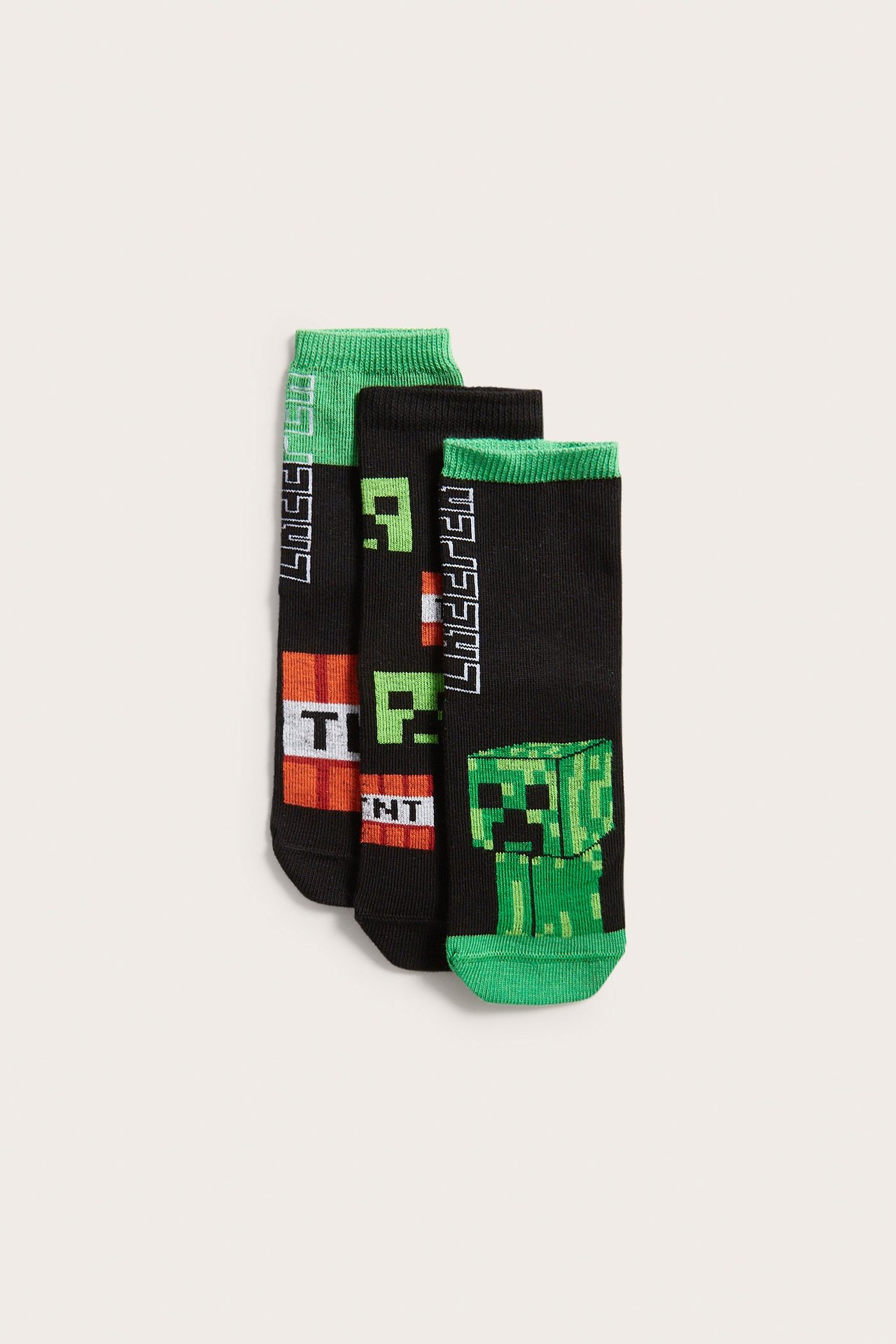 Widok z przodu trzech czarnych skarpet dziecięcych z zielonymi ściągaczami i nadrukami Minecraft.