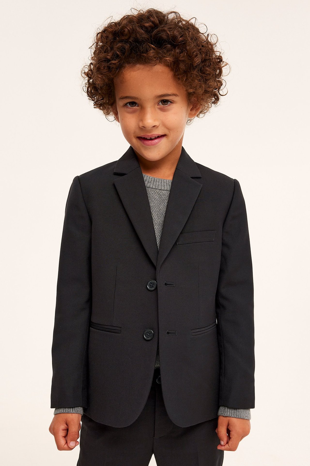 Frontvy av ett barn i en svart tvåknapps kavaj över en grå tröja och svarta byxor.