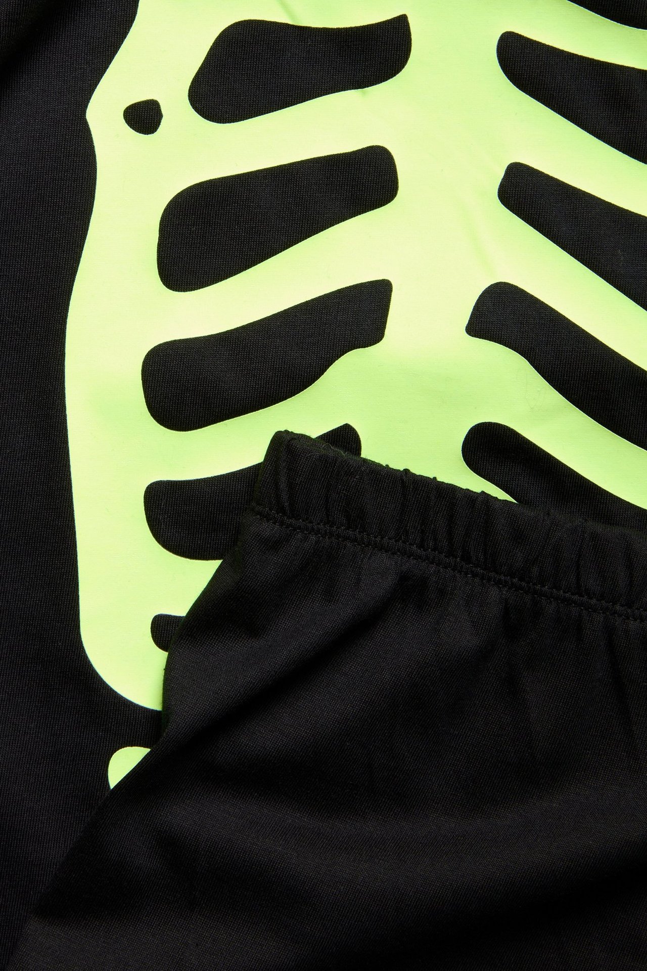 Zbliżenie na czarną bawełnianą piżamę dziecięcą z neonowo zielonym świecącym szkieletem i gumką w pasie.