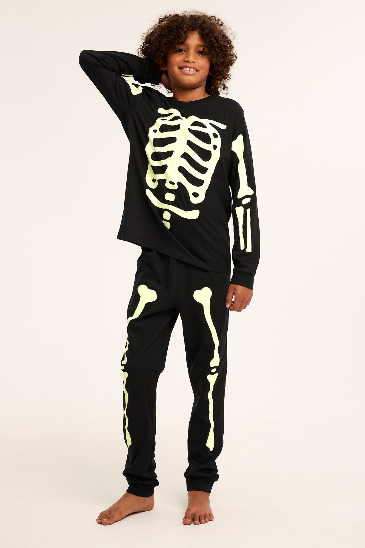 Edestä, lapsi mustassa puuvillapyjamassa, jossa hehkuva luurankokuvio.