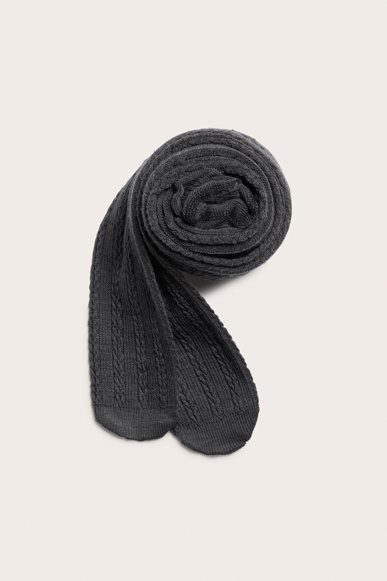 Ylhäältä näkymä tummanharmaista palmikkoneulotuista villasekoitesukkahousuista, rullattuina, jalka-osat näkyvissä.