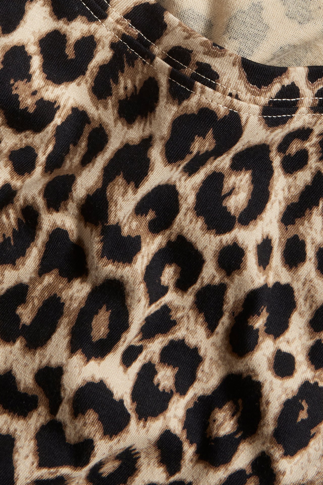 Närbild av en beige bomulls-t-shirt med brunt och svart leopardmönster och vita sömmar.