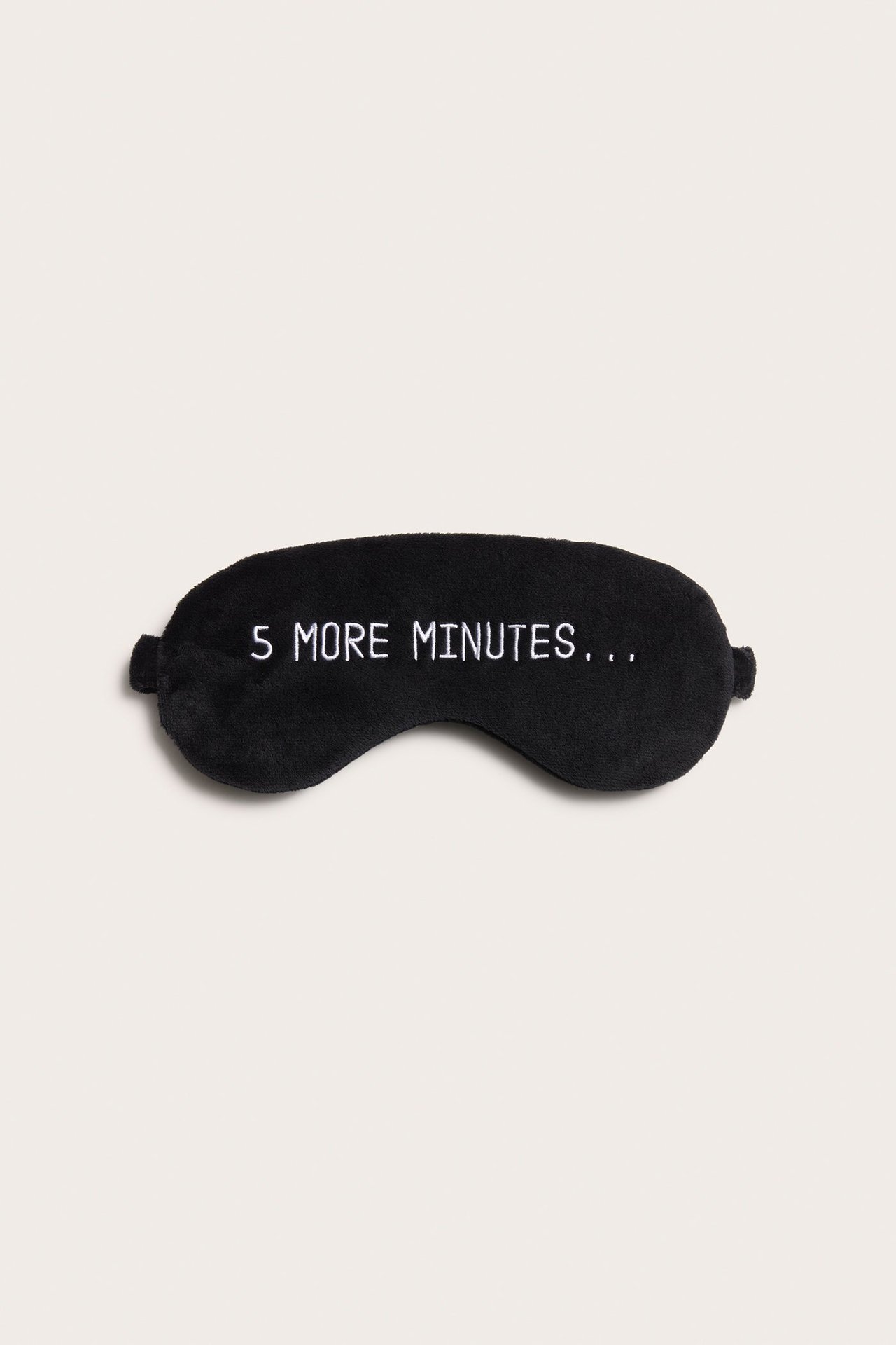 Widok z przodu czarnej welurowej maski do spania z białym haftem "5 MORE MINUTES..." i elastycznymi paskami.