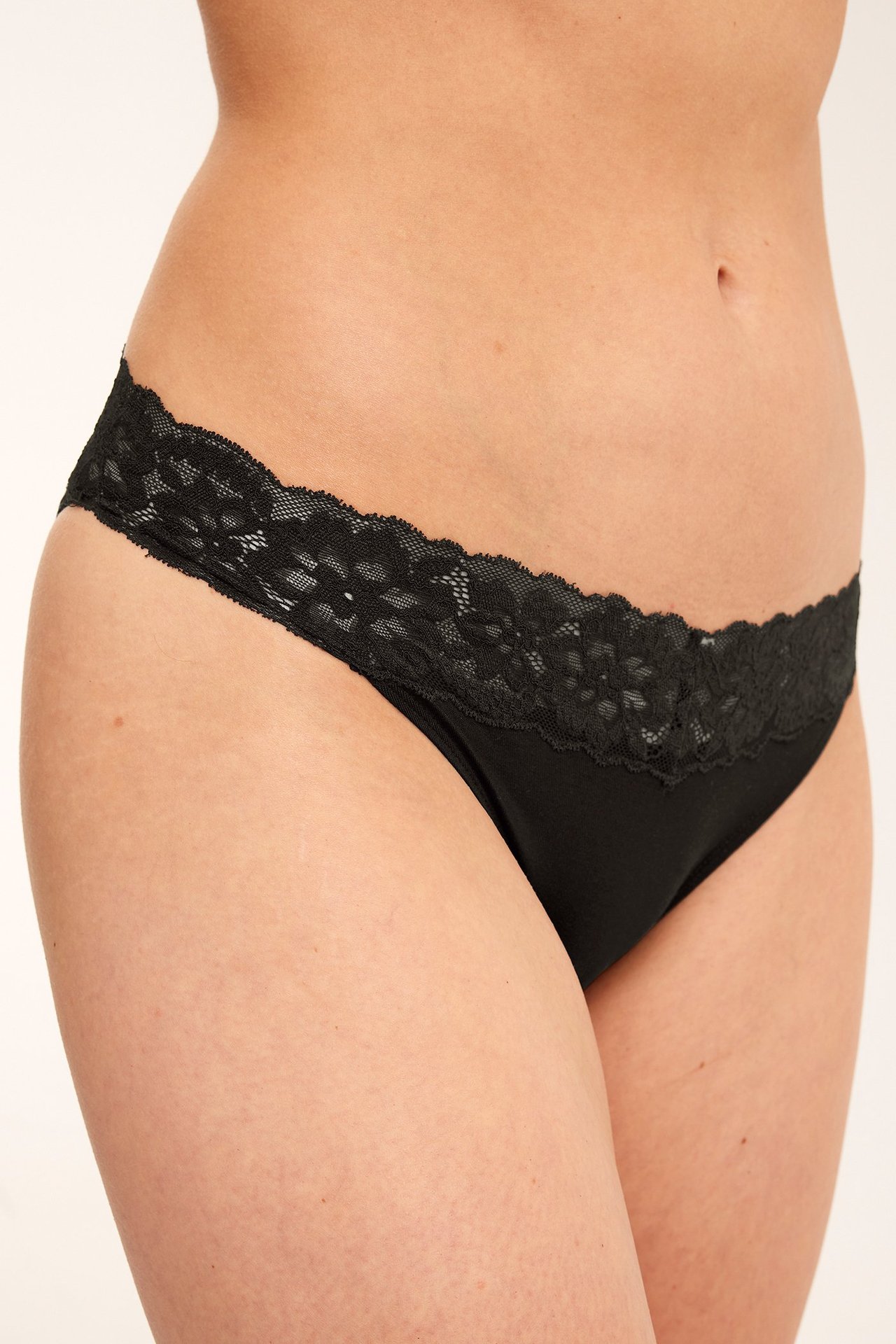 Närbild, sidovy av kvinna i svarta brazilian trosor i lyocell med dekorativ spetskant i midjan.