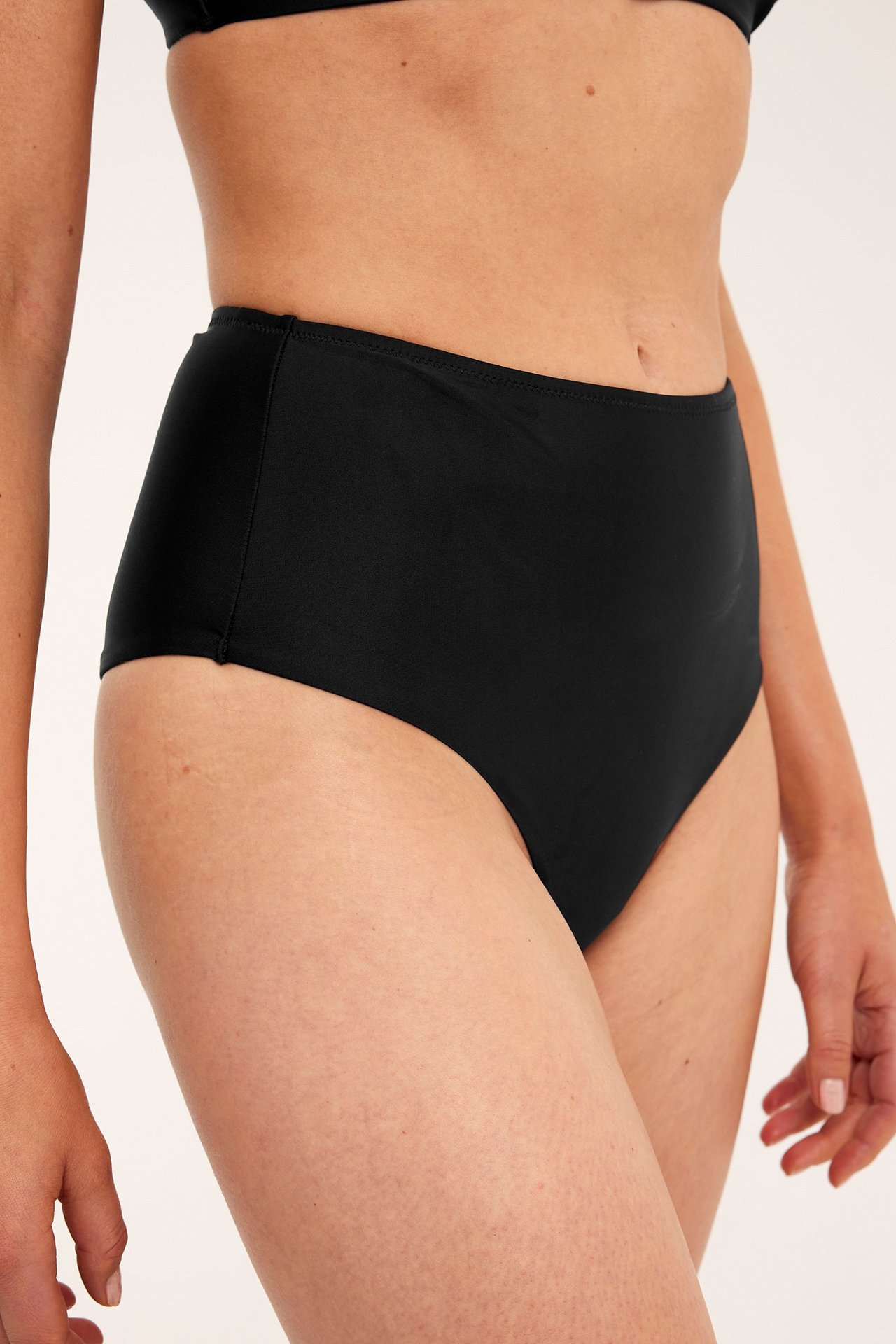 Sidebilde av en kvinne i svarte høy midje bikinitruse og en svart bikinitopp.