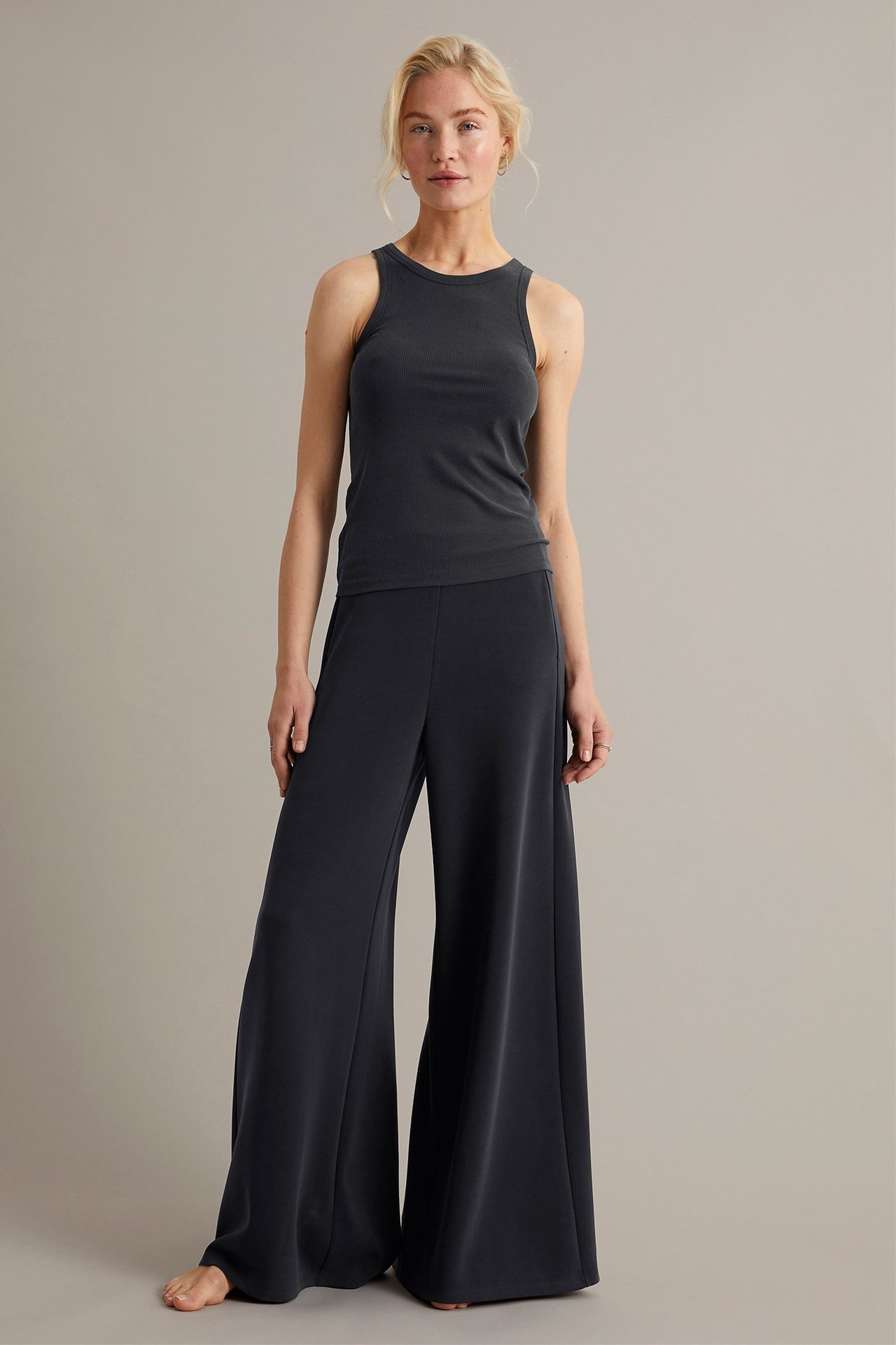 Forfra, kvinne i svart ettersittende singlet og svarte vide bukser.