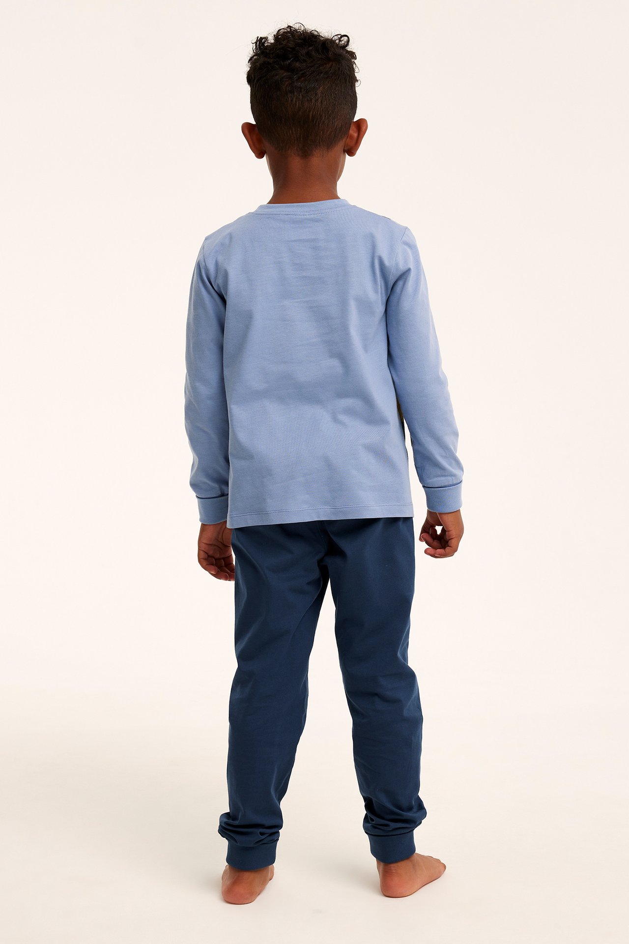 Bakfra, et barn i lyseblå langermet pyjamatopp og mørkeblå pyjamasbukser med ribbekanter.