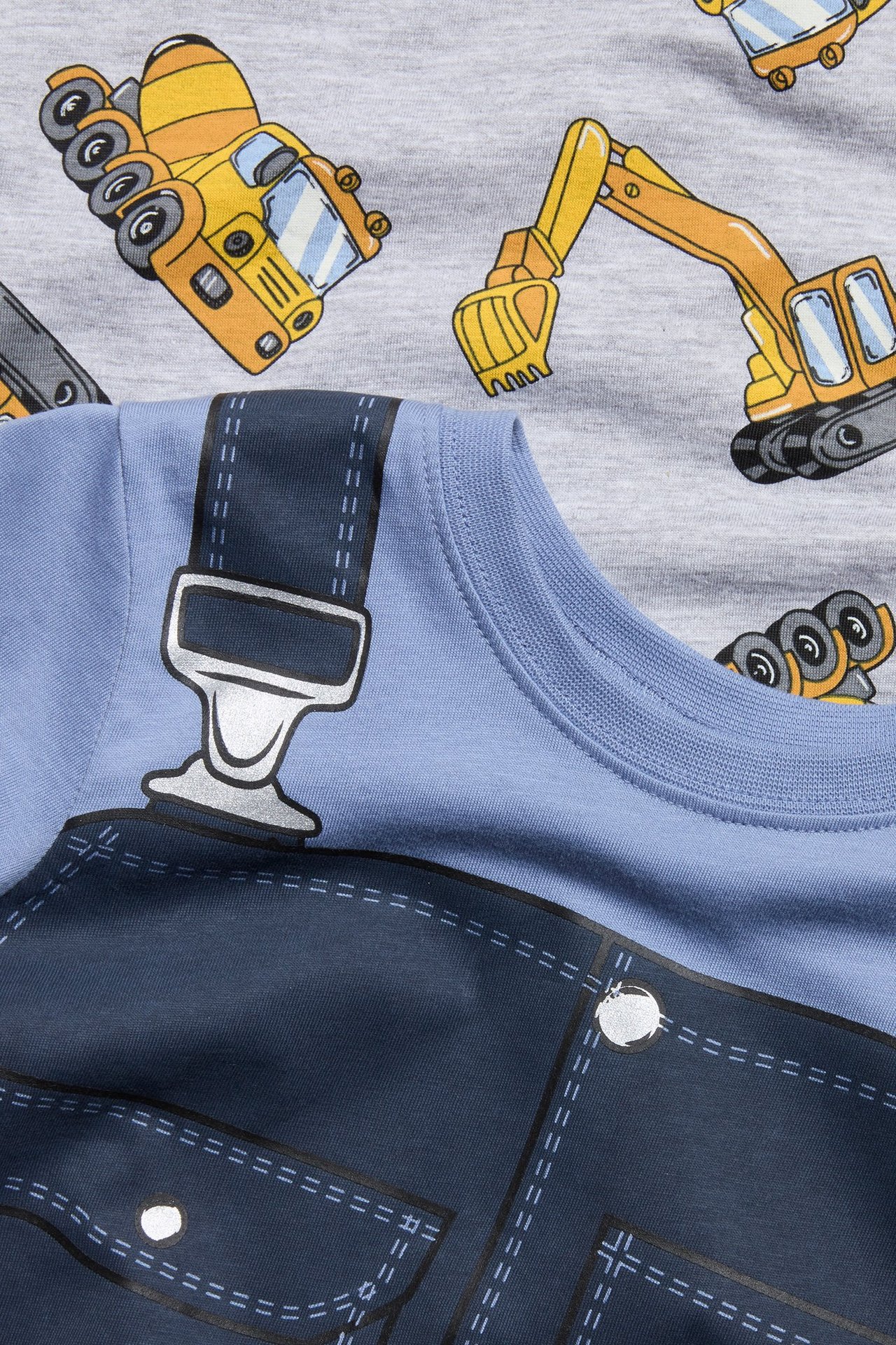 Zbliżenie na dziecięcą jasnoniebieską piżamową bluzkę z nadrukiem ogrodniczek i szarą bluzkę z wzorem pojazdów.