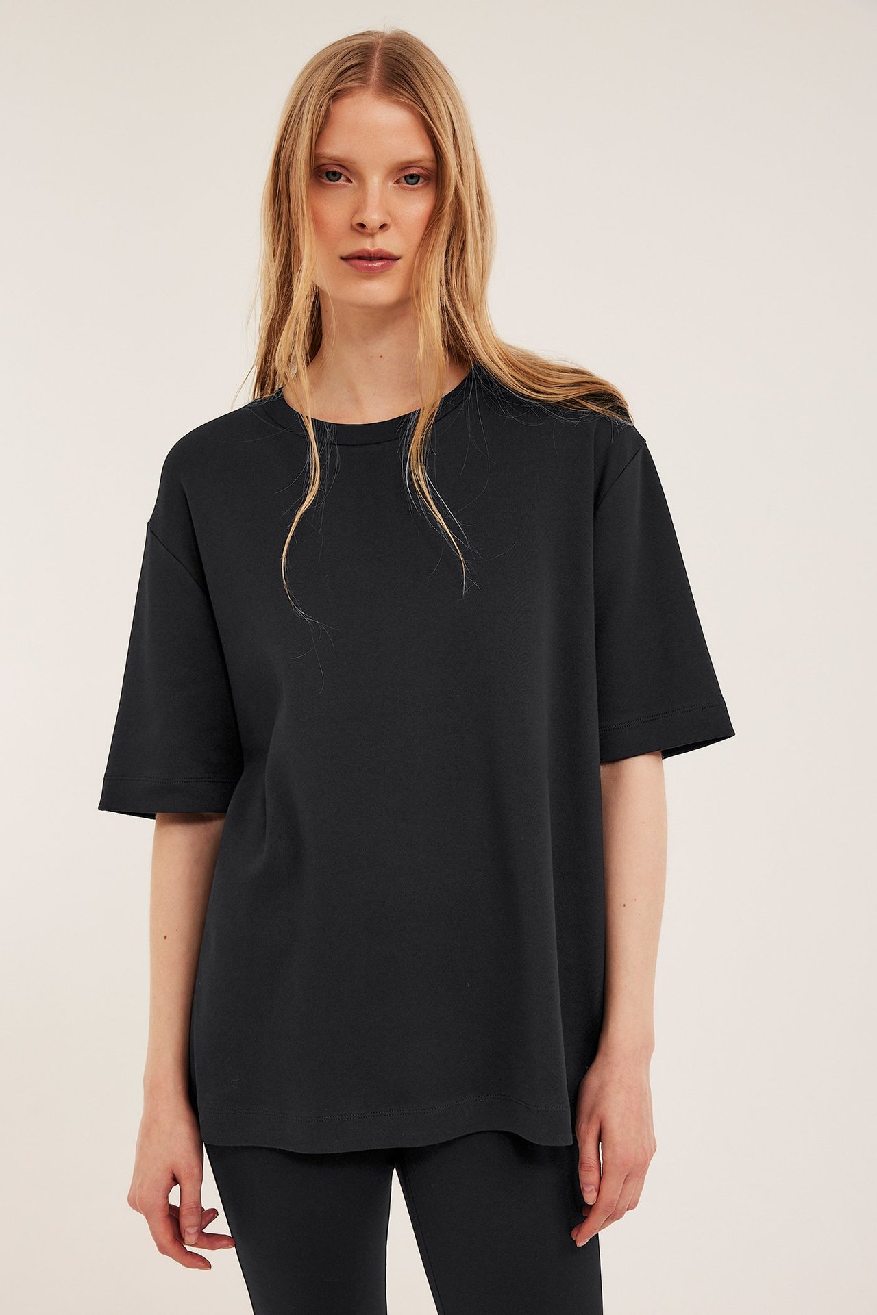 Frontvy av en kvinna i svart oversized t-shirt i interlock och svarta leggings.