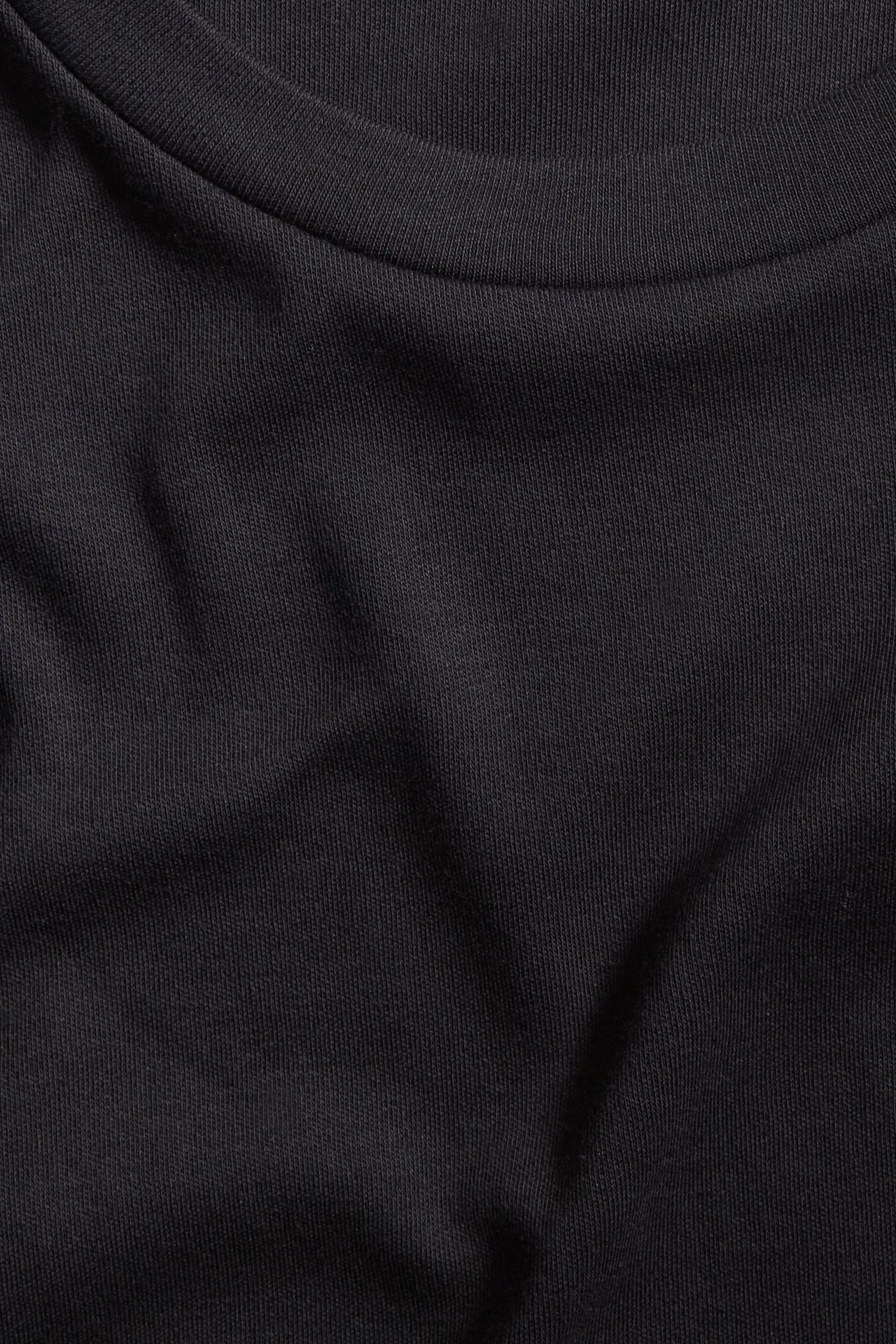 Zbliżenie czarnego, oversize'owego T-shirtu z bawełnianego interlocku, ukazujące jednolity materiał i dekolt.