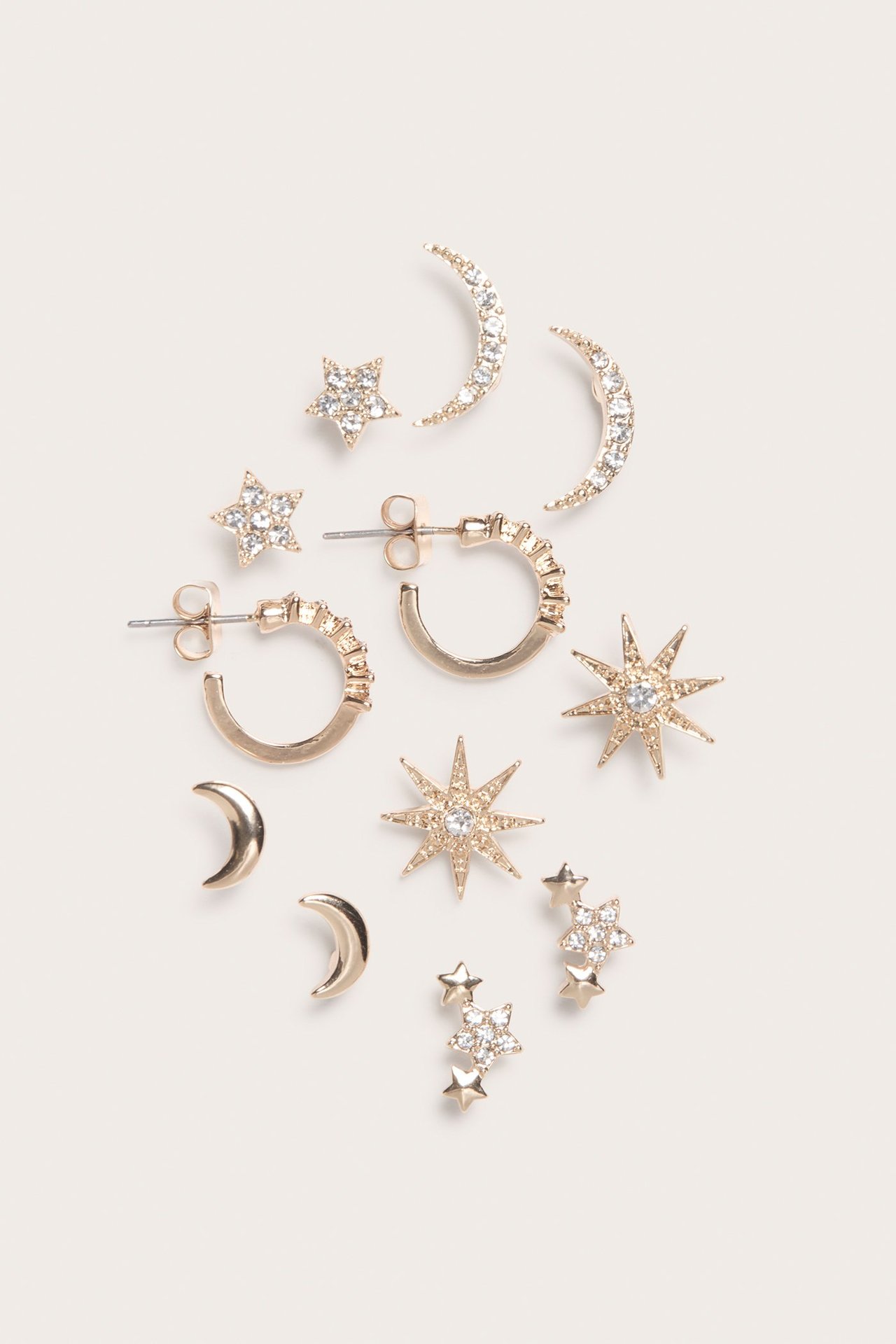 Zbliżenie sześciu par złotych kolczyków z detalami ze strasu, z motywami gwiazd, księżyców i kółek.