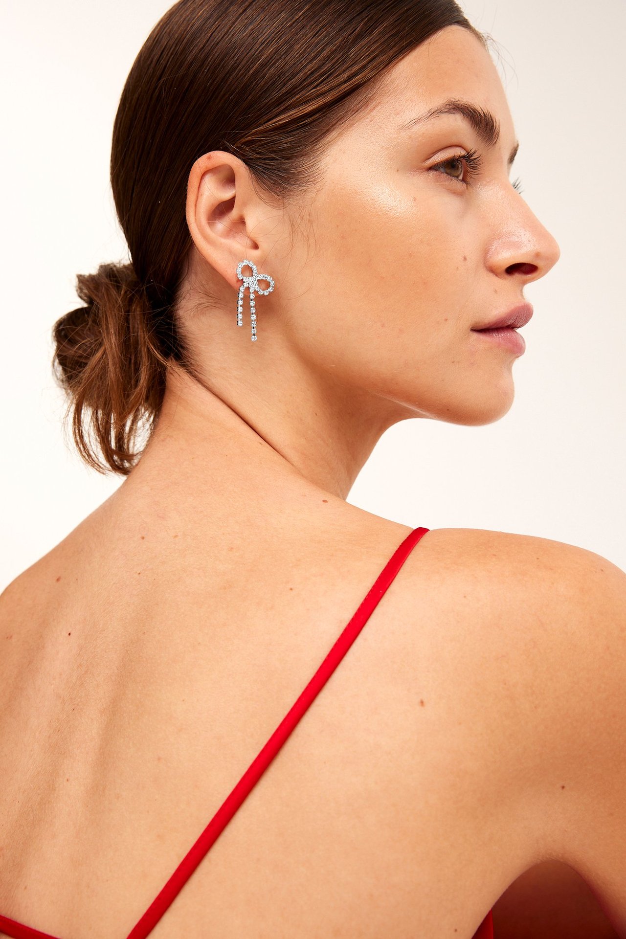 Zbliżenie z boku kobiety noszącej srebrne kolczyki w kształcie kokardek z cyrkoniami i czerwony top na ramiączkach.