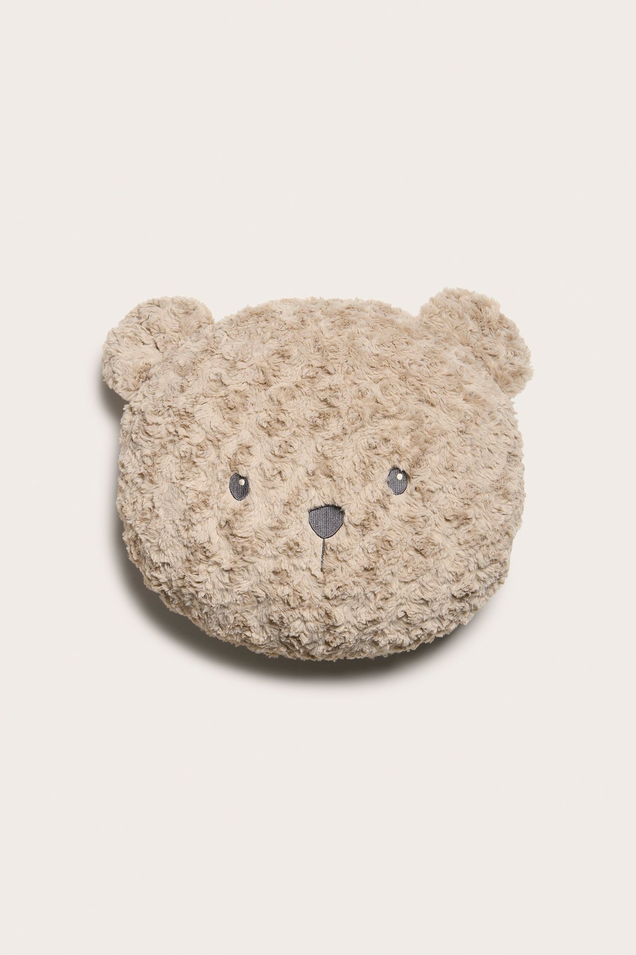Edestä: beige pörröinen nallepäätyyny, jossa on brodeeratut silmät ja nenä.